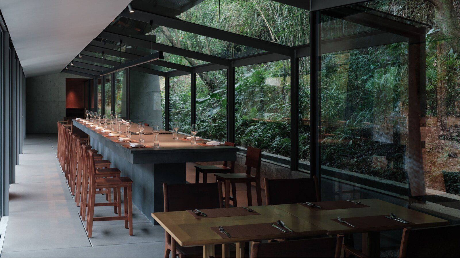 陽朔糖舍 Aurua 酒店的 Stream Restaurant，玻璃屋頂與玻璃牆外是整片竹林與綠色植物，室內一張長桌配紅木高腳椅