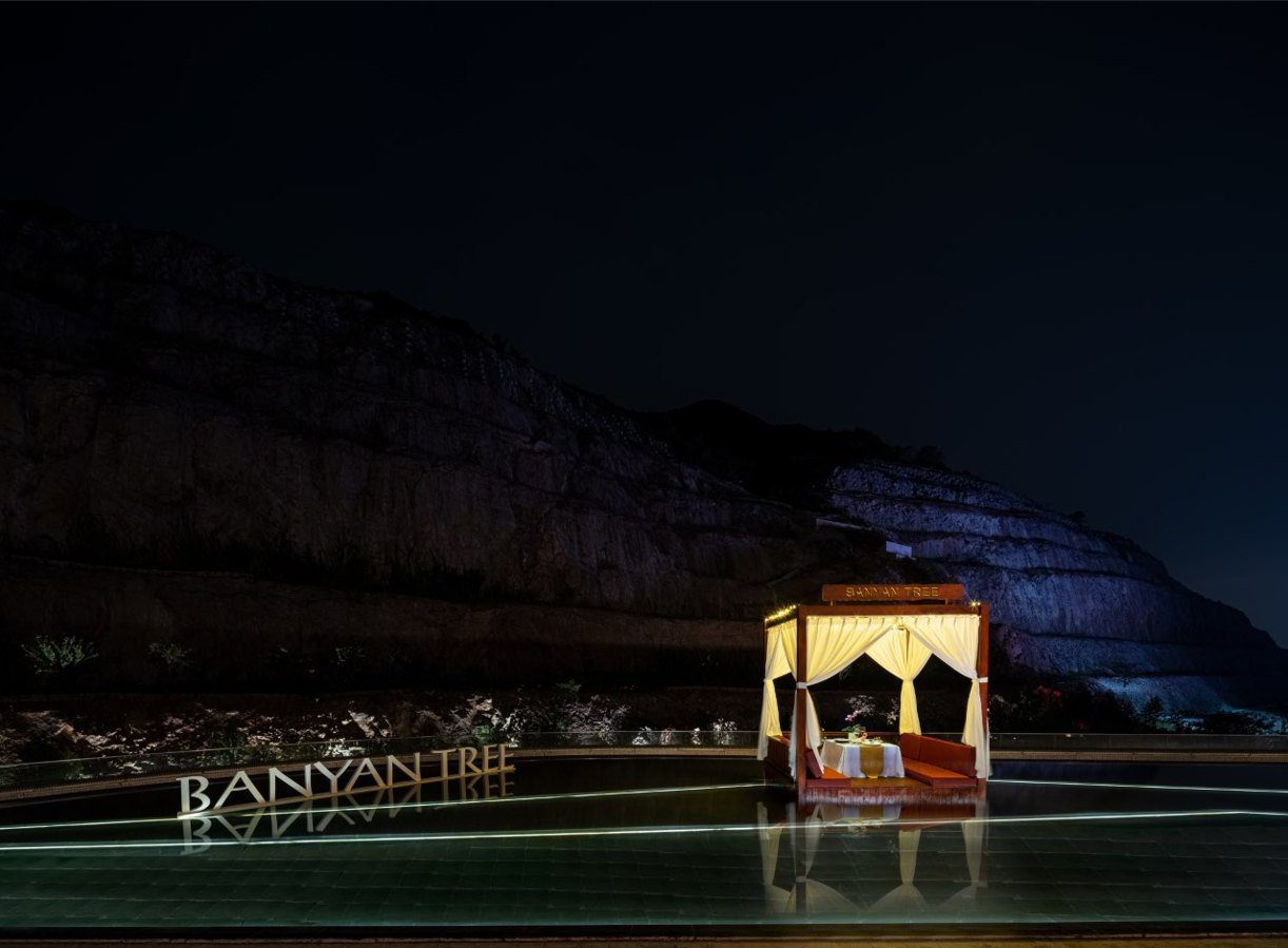 夜晚的水池邊立著 BANYAN TREE 字牌,一座掛著白色紗簾的亭子裡擺著餐桌,後方是黑暗中的採石場岩壁