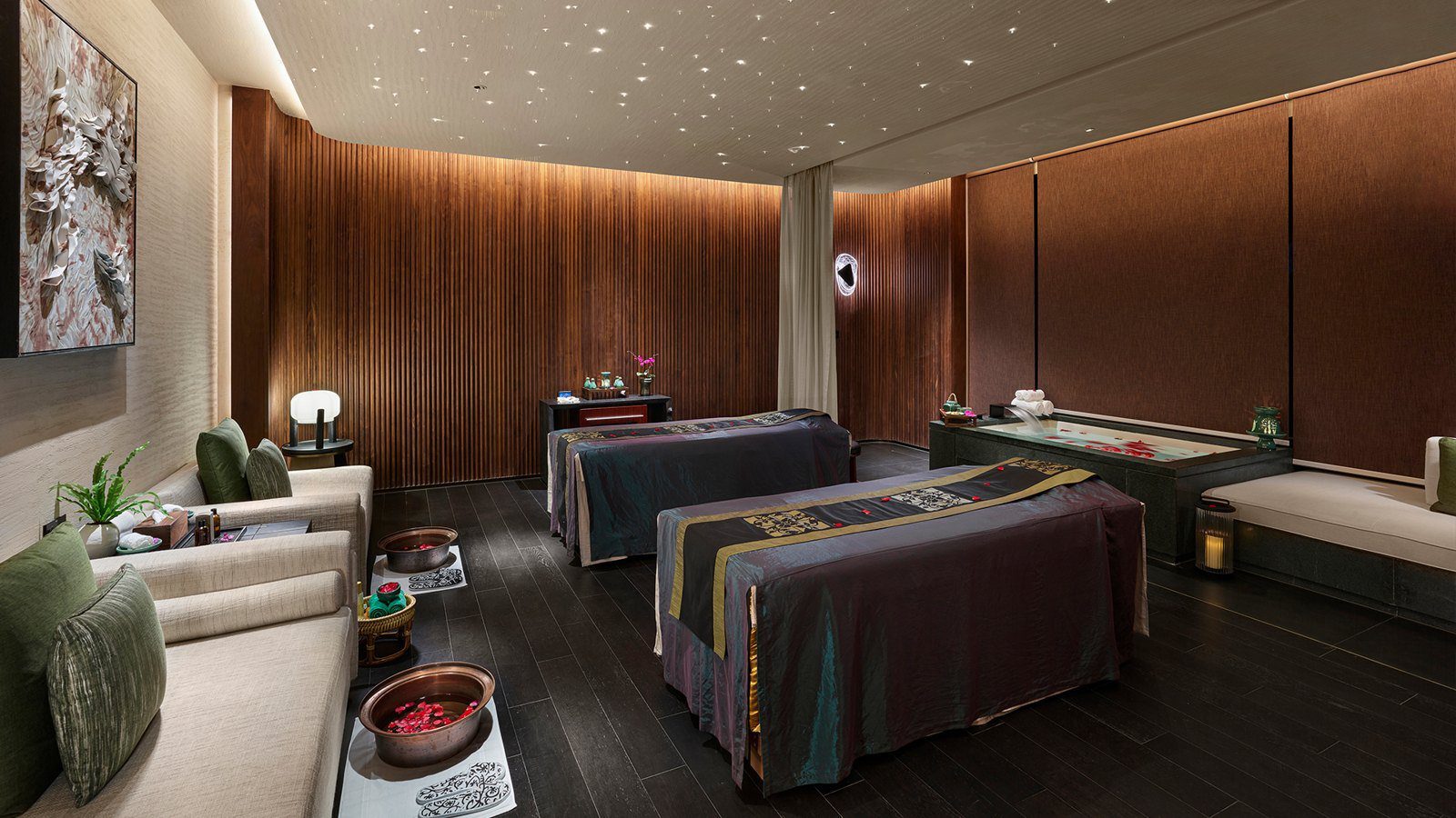 南京園博園悅榕莊酒店悅榕 SPA 的雙人護理室，兩張按摩床並排，右側是撒著花瓣的浴池，天花板點綴星點燈光