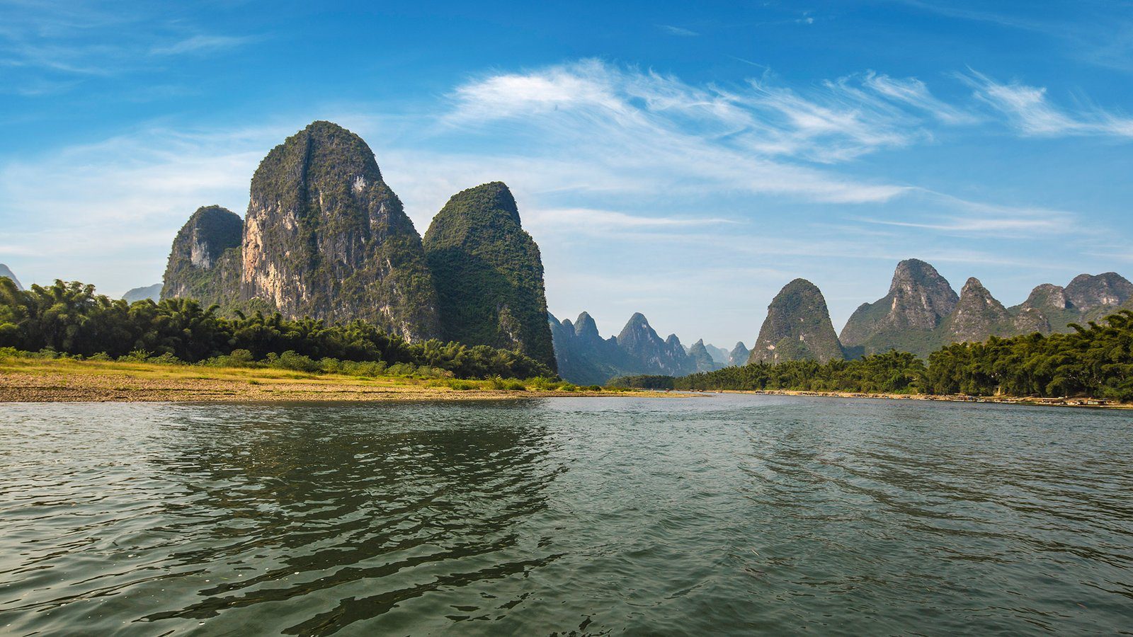 陽朔周邊的漓江風景，晴天下江面寬闊，岸邊是竹林與一座座陡峭的喀斯特山峰