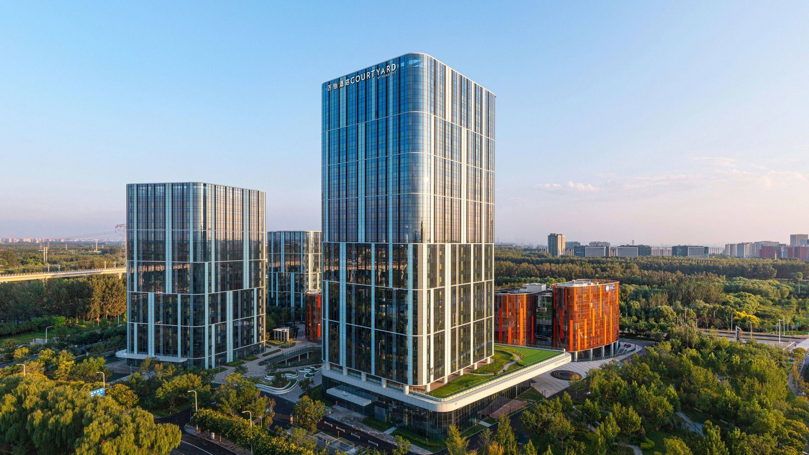 北京未來科學城萬怡酒店的空拍外觀，玻璃塔樓頂端有 COURTYARD 招牌，周圍是其他辦公樓與大片樹林
