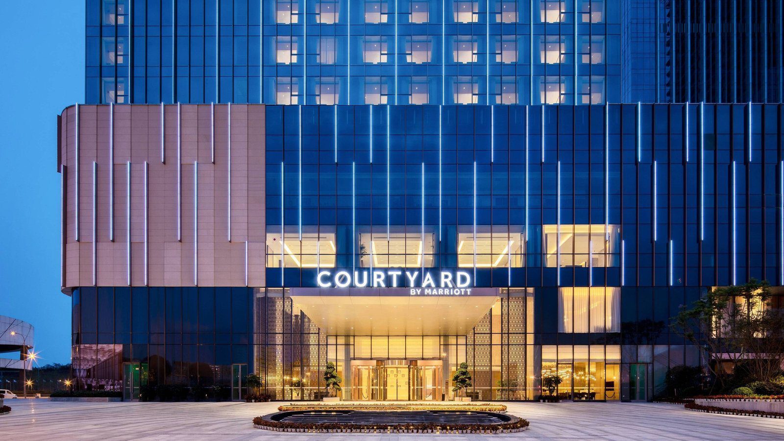成都天投萬怡酒店的入口夜景，玻璃帷幕上亮著 COURTYARD BY MARRIOTT 招牌，門廊下是旋轉門，前方是圓形水景