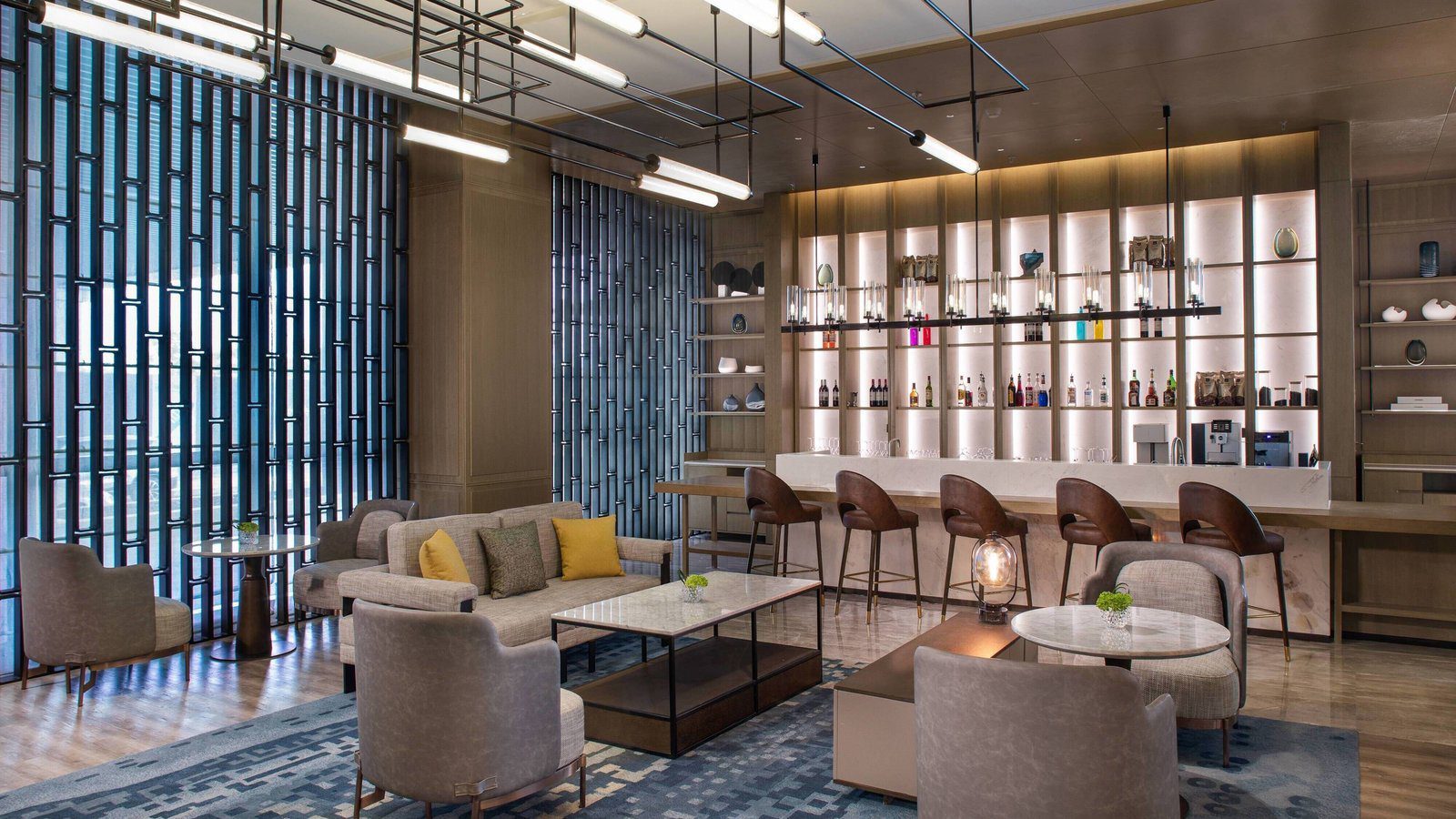 成都天投萬怡酒店的大堂吧 The Lounge，發光層架前是吧檯與皮革高腳椅，前方是沙發與大理石茶几