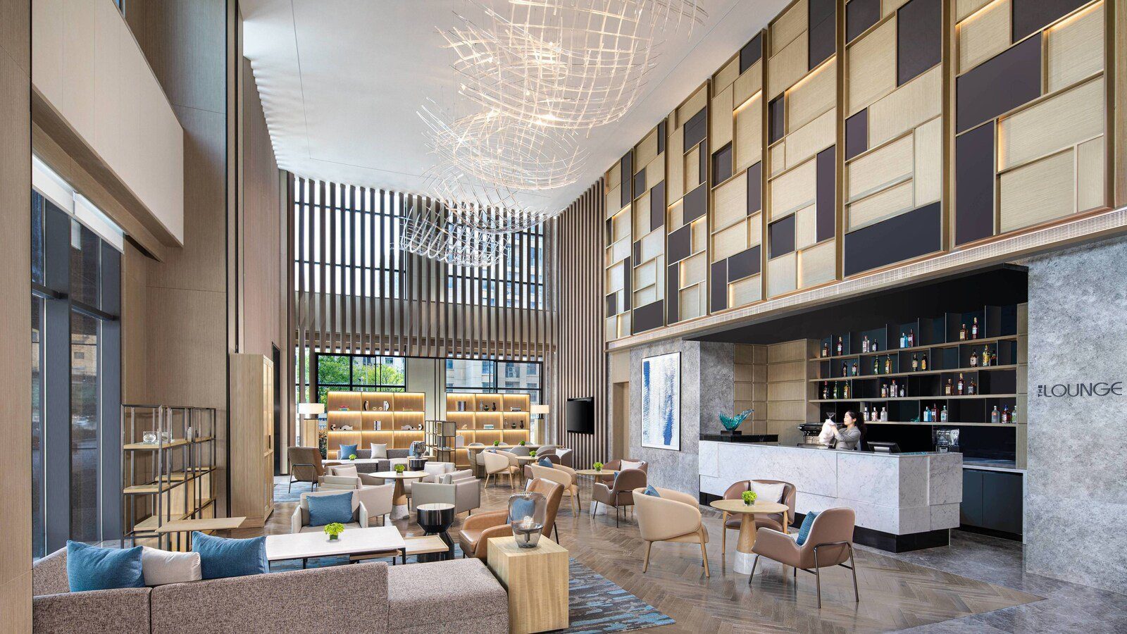 南京金輪萬怡酒店挑高的大堂吧，吧台旁牆上寫著 THE LOUNGE，前方擺著沙發與扶手椅
