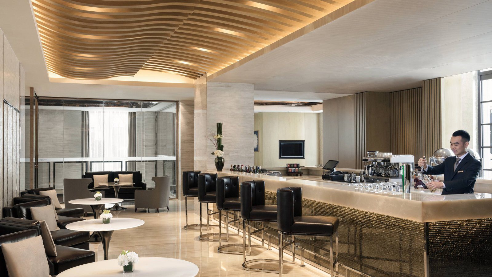 上海蘇寧環球萬怡酒店的 The Lounge 大堂吧，波浪木條天花下是發光吧檯與黑色高腳椅，左側是皮沙發座