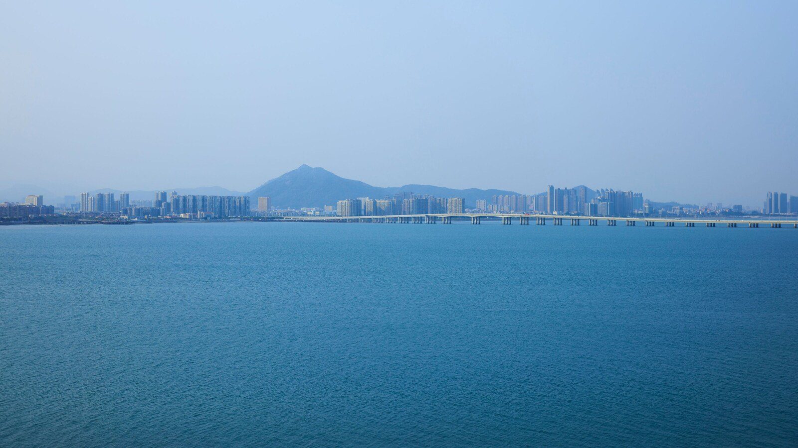 廈門百琪萬怡酒店周邊的海景,藍色海面對岸是一排高樓與一座山,右側是跨海大橋