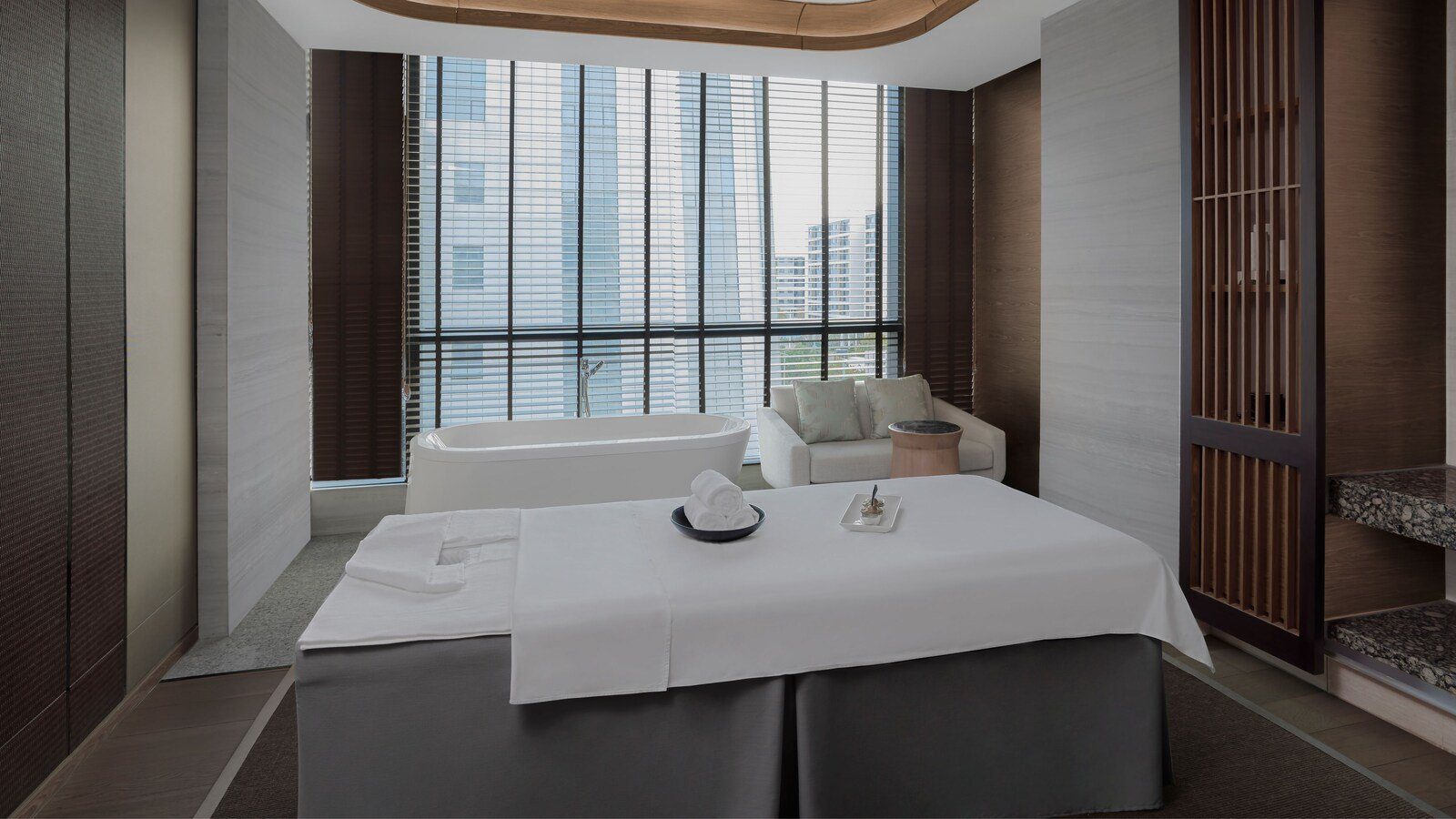 廈門百琪萬怡酒店的沁 SPA 護理室，白色護理床後方是獨立浴缸與沙發，窗前拉著百葉簾