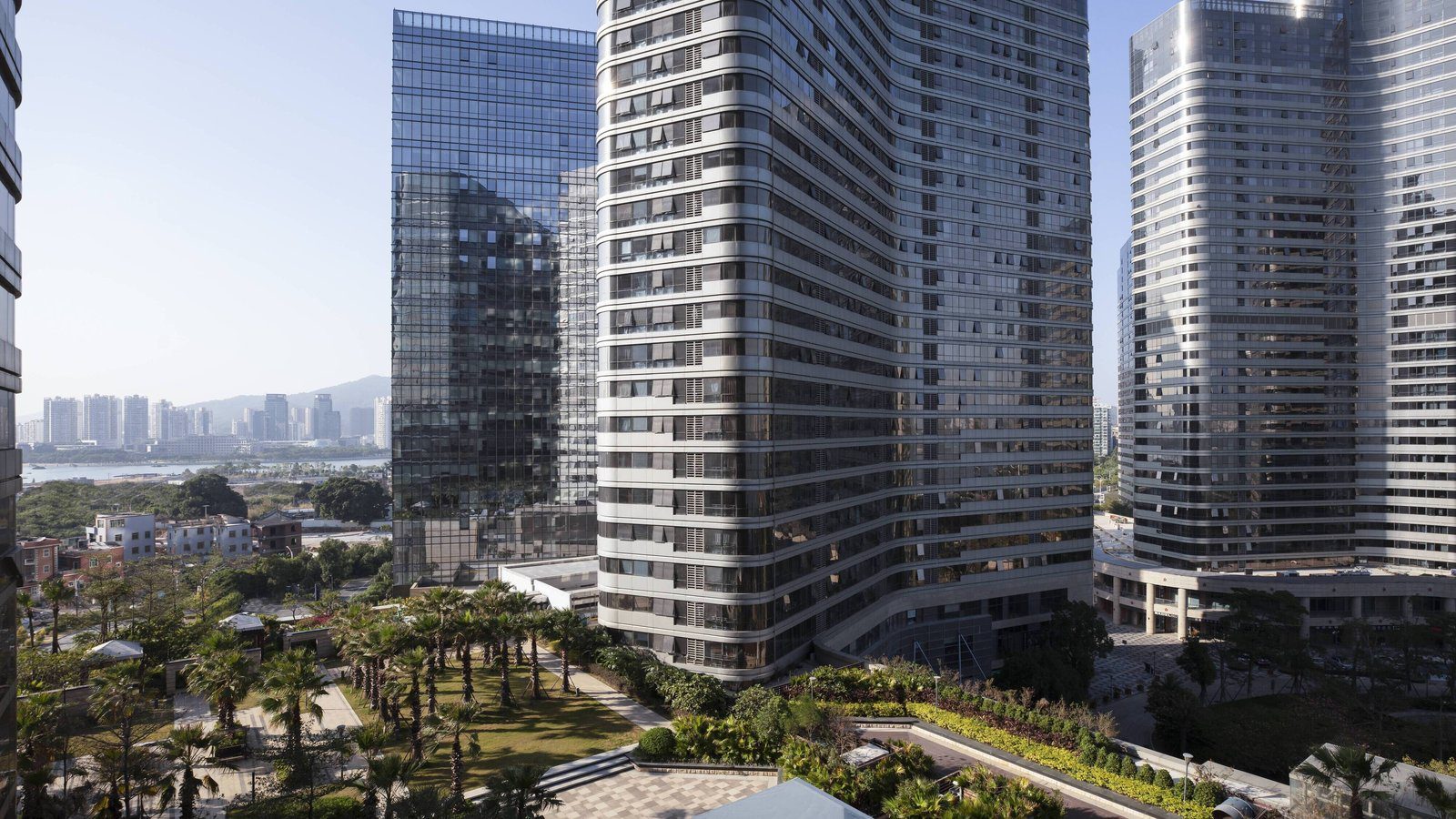 廈門泰地萬怡酒店周邊景觀,幾棟玻璃帷幕高樓之間是種滿棕櫚樹的綠地,遠方是水面與山