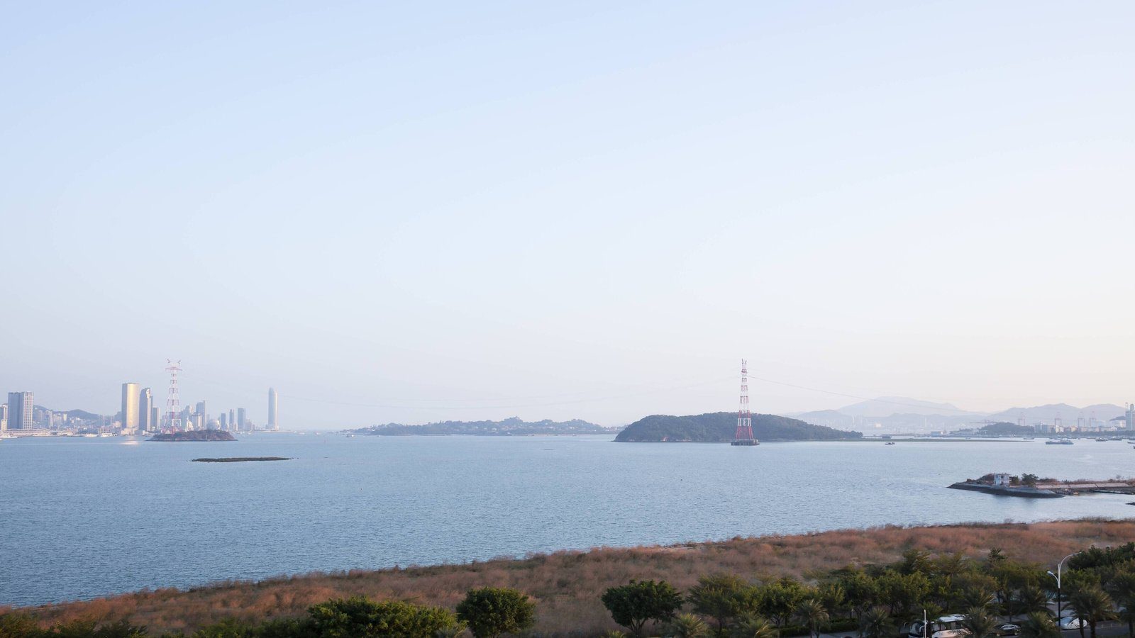 廈門泰地萬怡酒店周邊景觀，從高處望向海面、小島與遠方的高樓，前景是岸邊草地與樹木