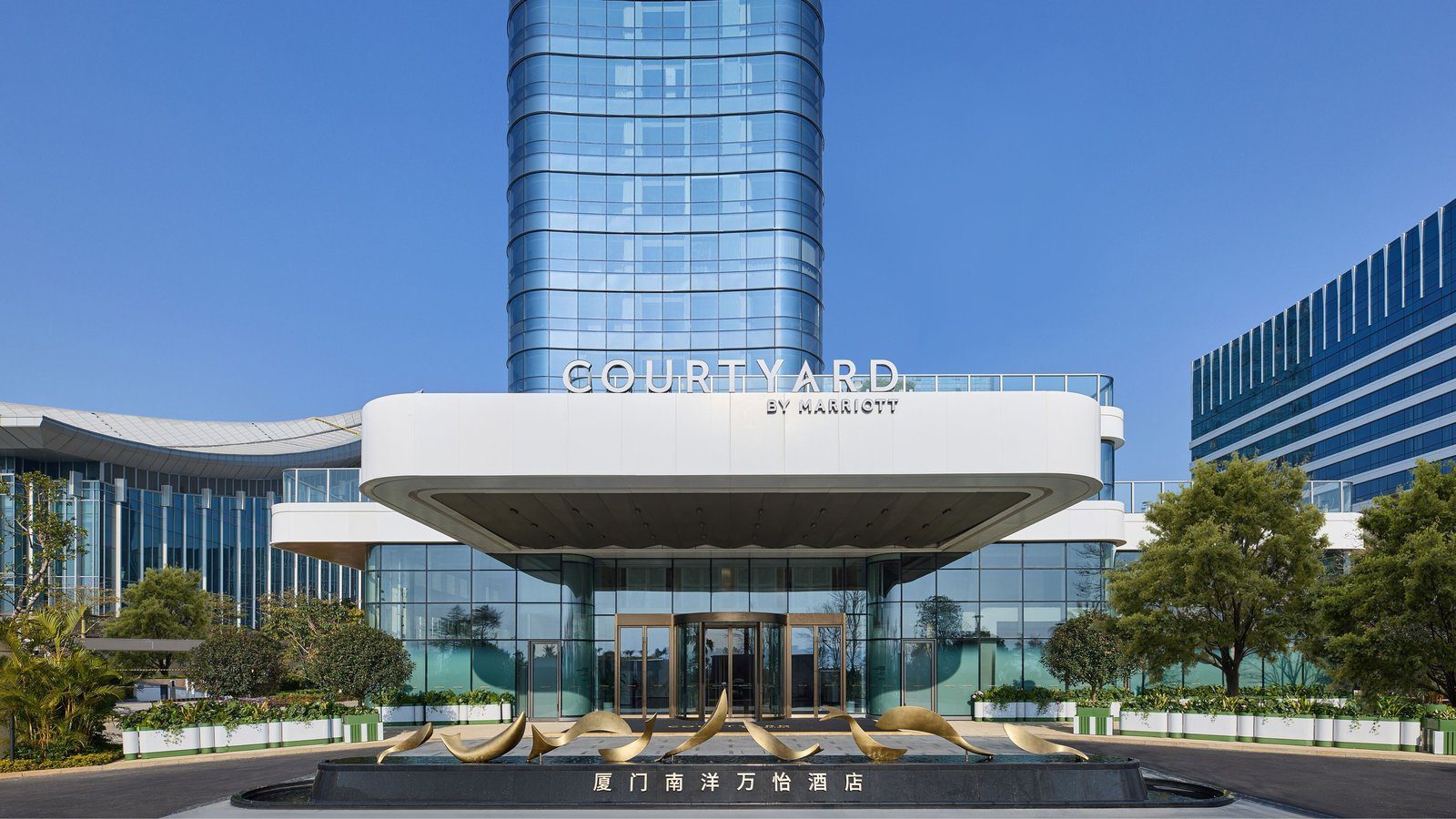 廈門南洋萬怡酒店的入口，白色弧形雨遮上方是 COURTYARD BY MARRIOTT 招牌，前方水景立牌寫著館名