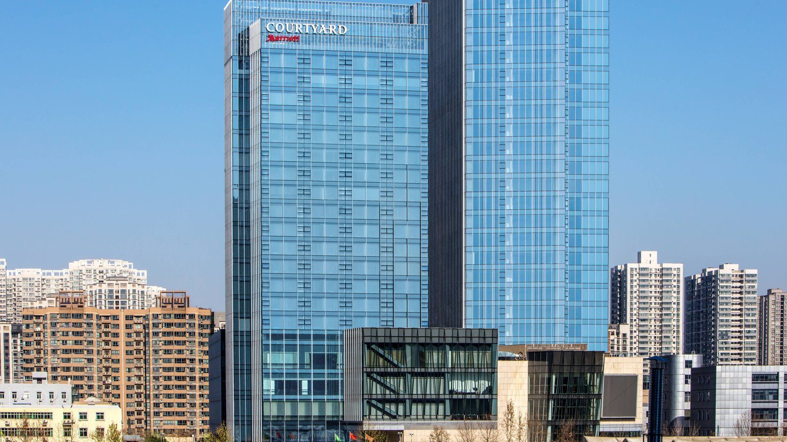 西安藍海風萬怡酒店白天的外觀,藍色玻璃帷幕塔樓頂端是 COURTYARD 招牌,兩側是住宅大樓