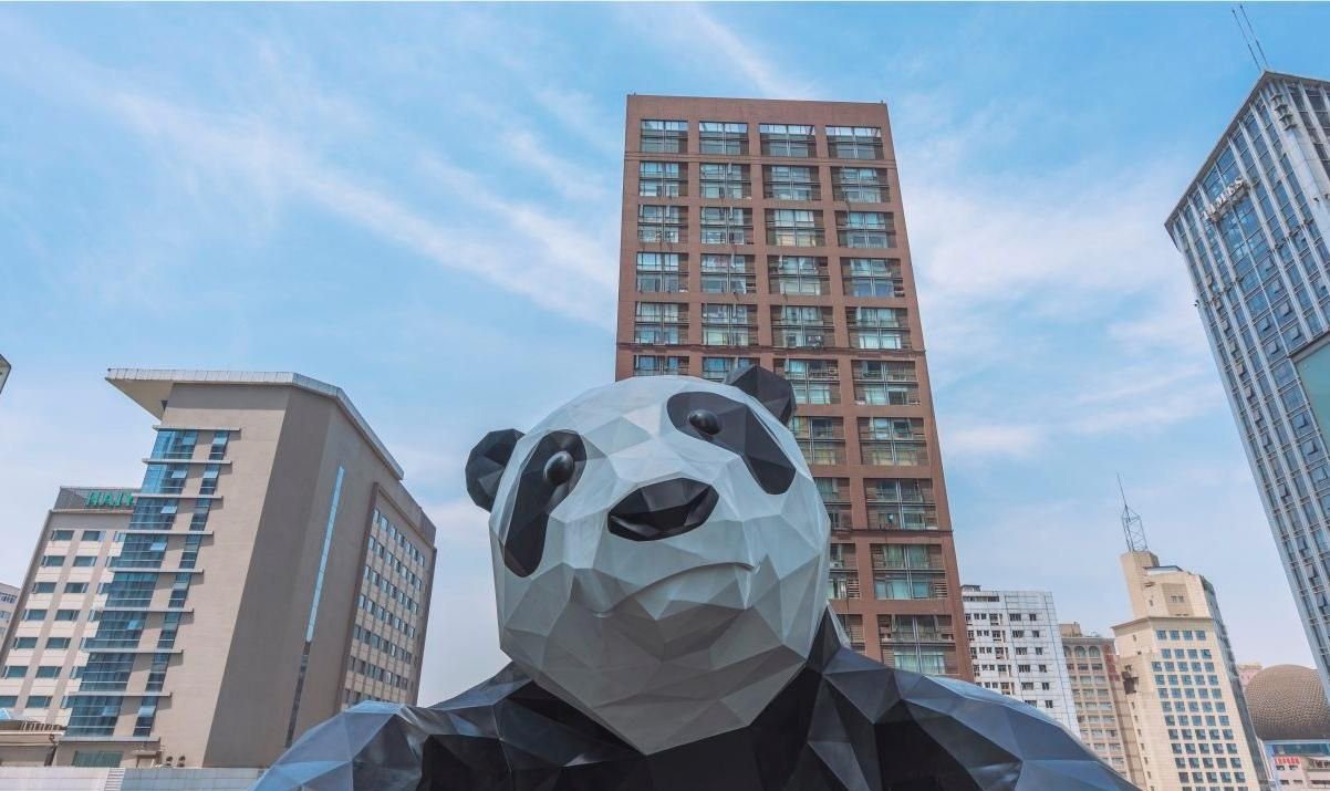 成都 IFS 外牆上的巨型攀爬熊貓雕塑 I'm Here 仰角近景，背後是春熙路商圈的紅磚色高樓與辦公大樓，距飯店約 0.2 公里