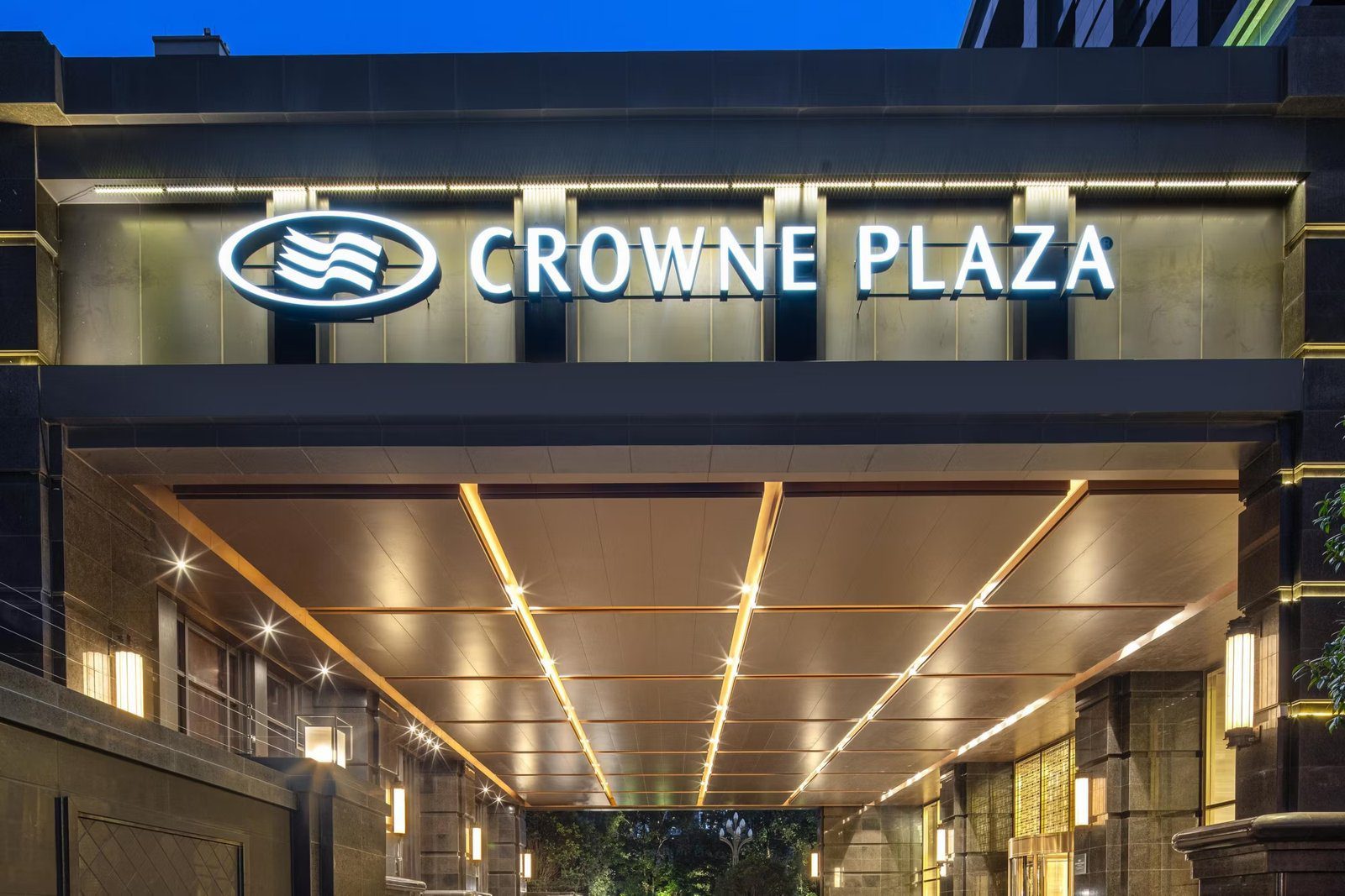 夜間的成都天府皇冠假日酒店車道入口,上方是 CROWNE PLAZA 發光招牌,雨遮天花有金色燈條,車道兩側是石材牆面與壁燈