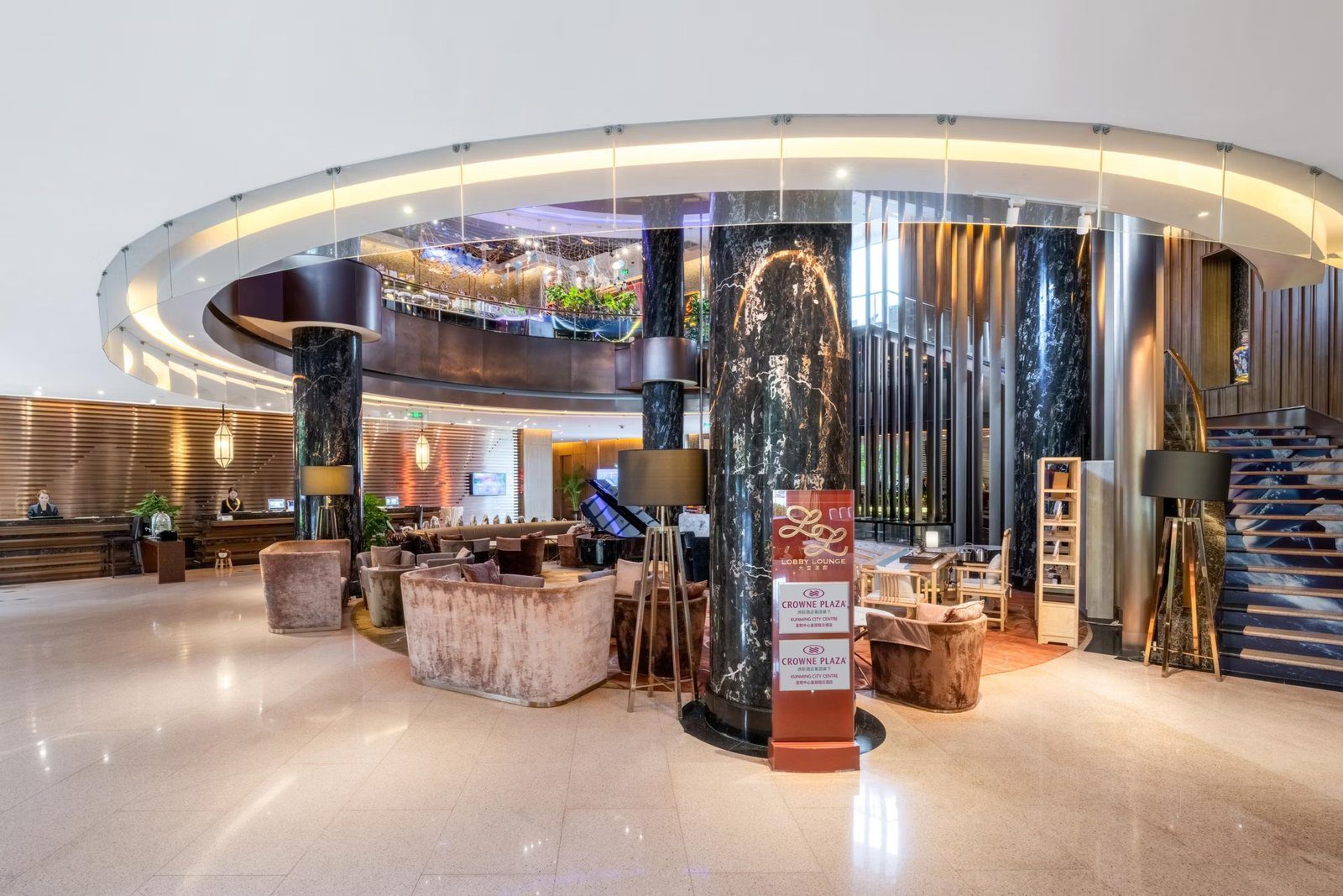 昆明中心皇冠假日酒店大堂,黑色大理石圓柱圍著大堂酒廊的絨布沙發,上方是環形挑空與二樓中庭