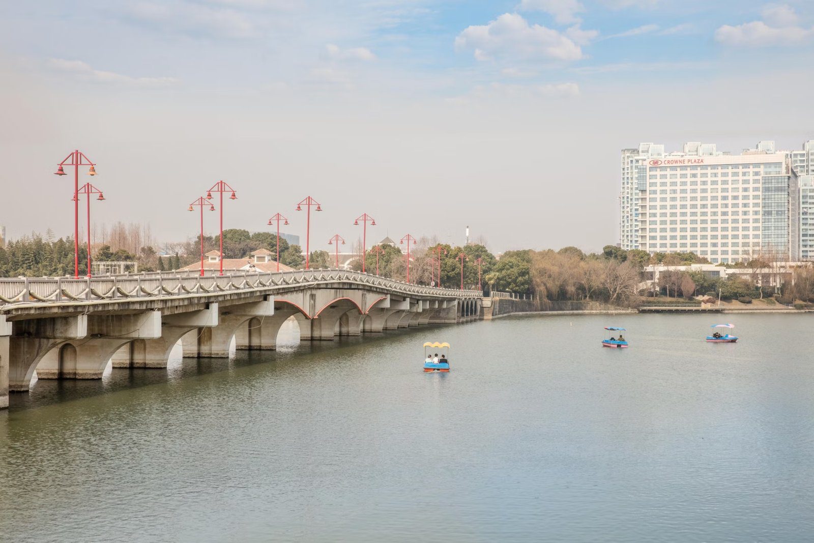 百家湖上的拱橋與腳踏船，右側湖岸是掛著 CROWNE PLAZA 招牌的南京銀城皇冠假日酒店