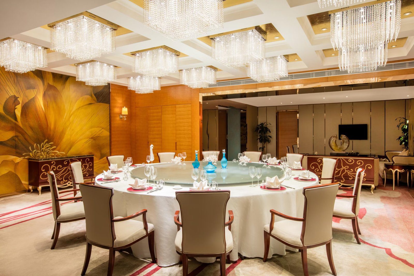 南京銀城皇冠假日酒店百家樓中餐廳包廂，水晶吊燈下是擺好餐具的大圓桌，牆上是金黃色花卉壁畫
