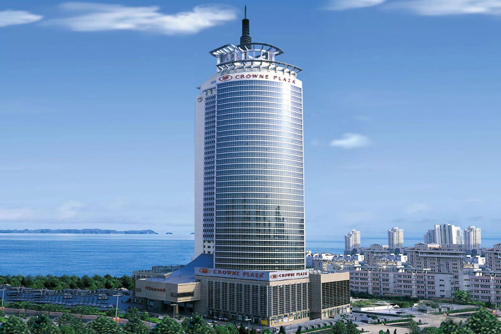 青島頤中皇冠假日酒店白天外觀,圓柱形塔樓後方是海面與遠方的山