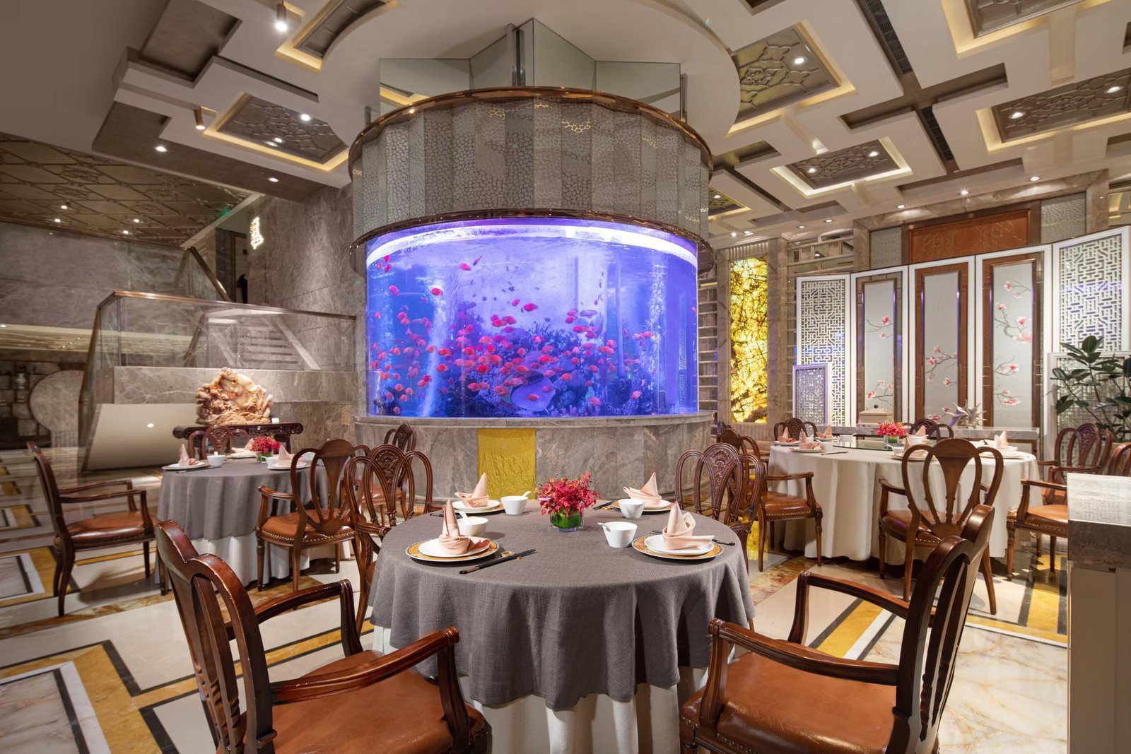 上海南新雅皇冠假日酒店中餐廳用餐區的圓柱形海水魚缸、圓桌與中式木椅