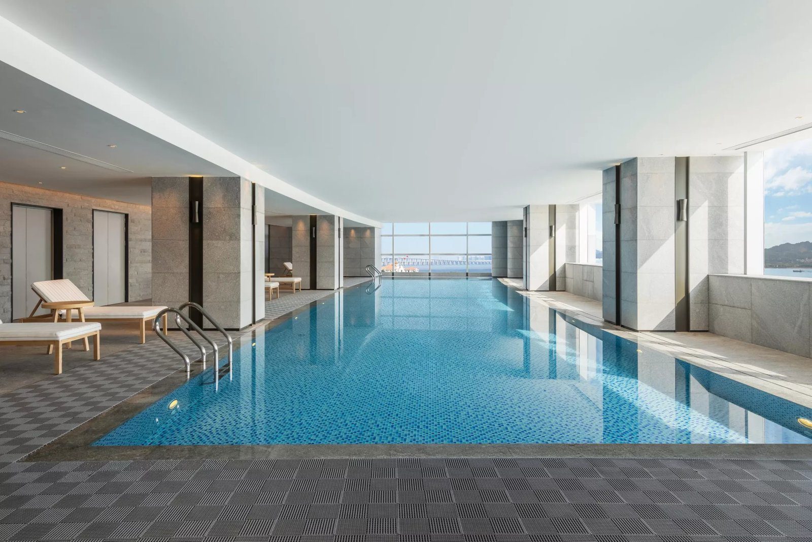廈門集美海景皇冠假日酒店室內泳池：藍色池水沿落地窗延伸，池畔設躺椅