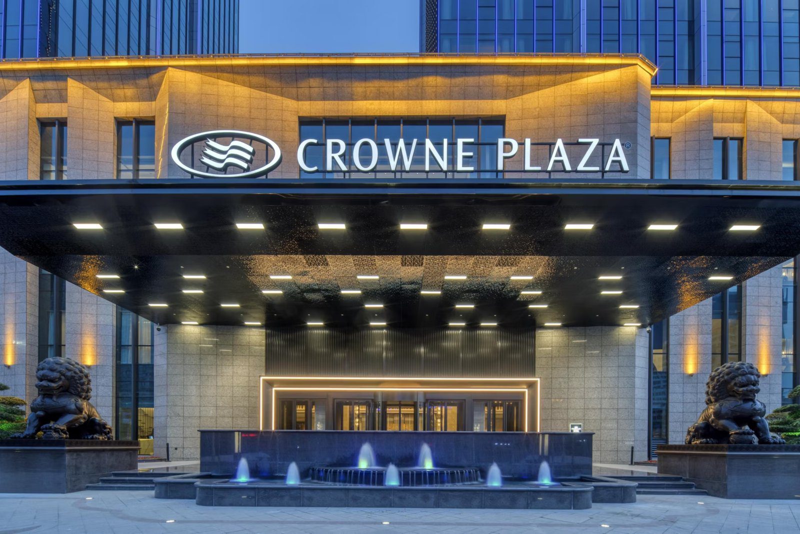 西安廣成皇冠假日酒店主入口，黑色雨遮上方掛著 CROWNE PLAZA 招牌，門前有噴泉水池，兩側各坐著一隻石獅