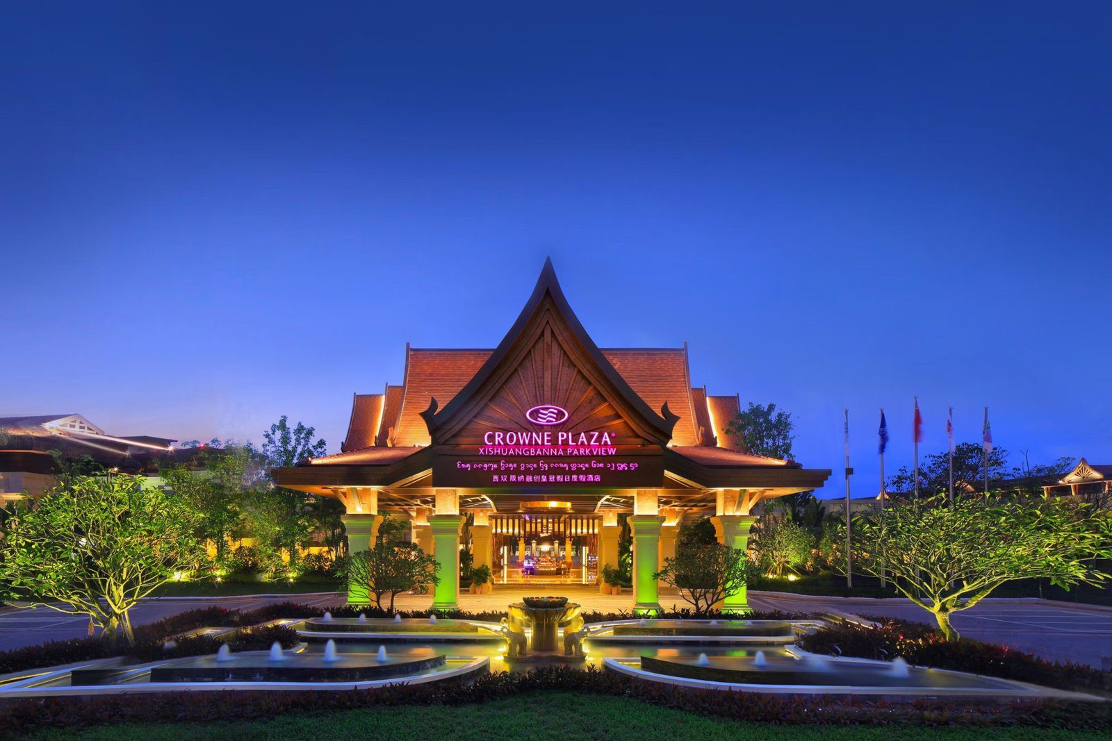 夜晚亮燈的傣式門廊,屋簷下掛著 CROWNE PLAZA XISHUANGBANNA PARKVIEW 招牌,前方是大象雕像噴泉