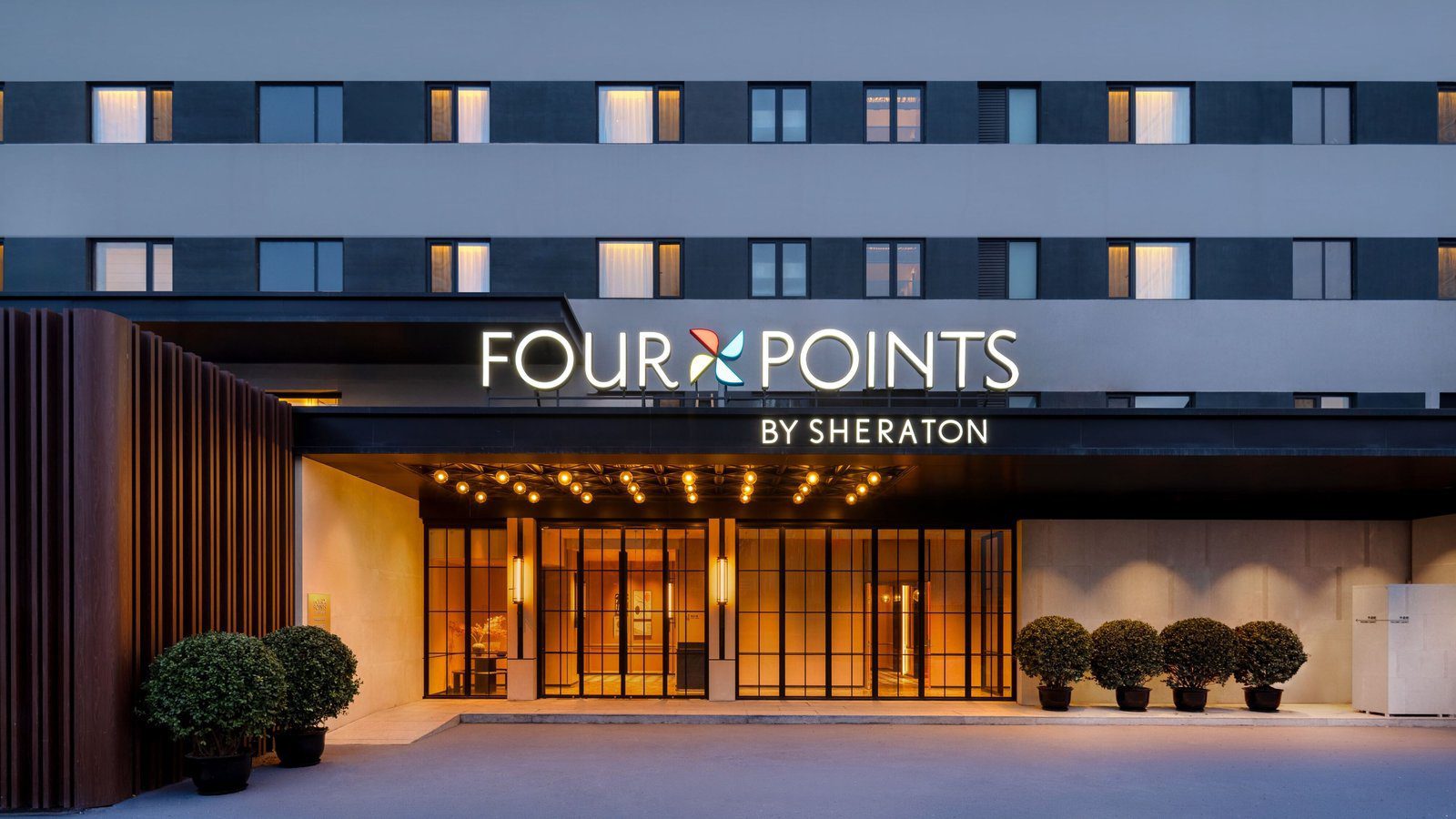 北京西站福朋喜來登酒店的入口，雨遮上亮著 FOUR POINTS BY SHERATON 招牌，玻璃門兩側擺著盆栽