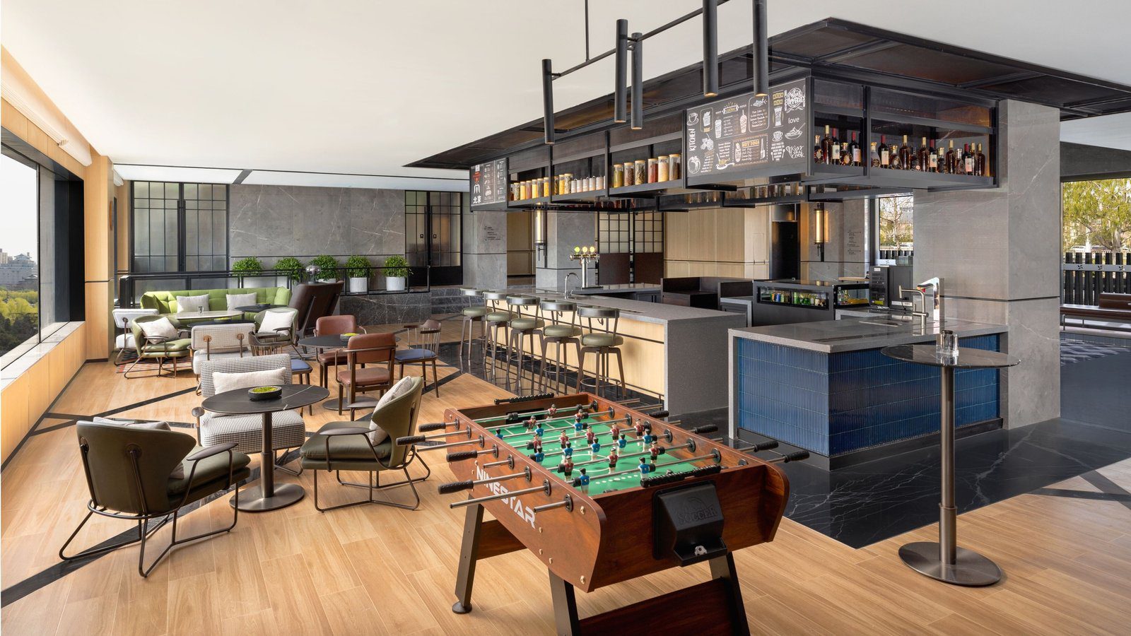 北京西站福朋喜來登酒店的 The Mesh Bar，前方是手足球台，後方是懸吊酒櫃下的吧台與高腳椅，左側大窗外是綠樹