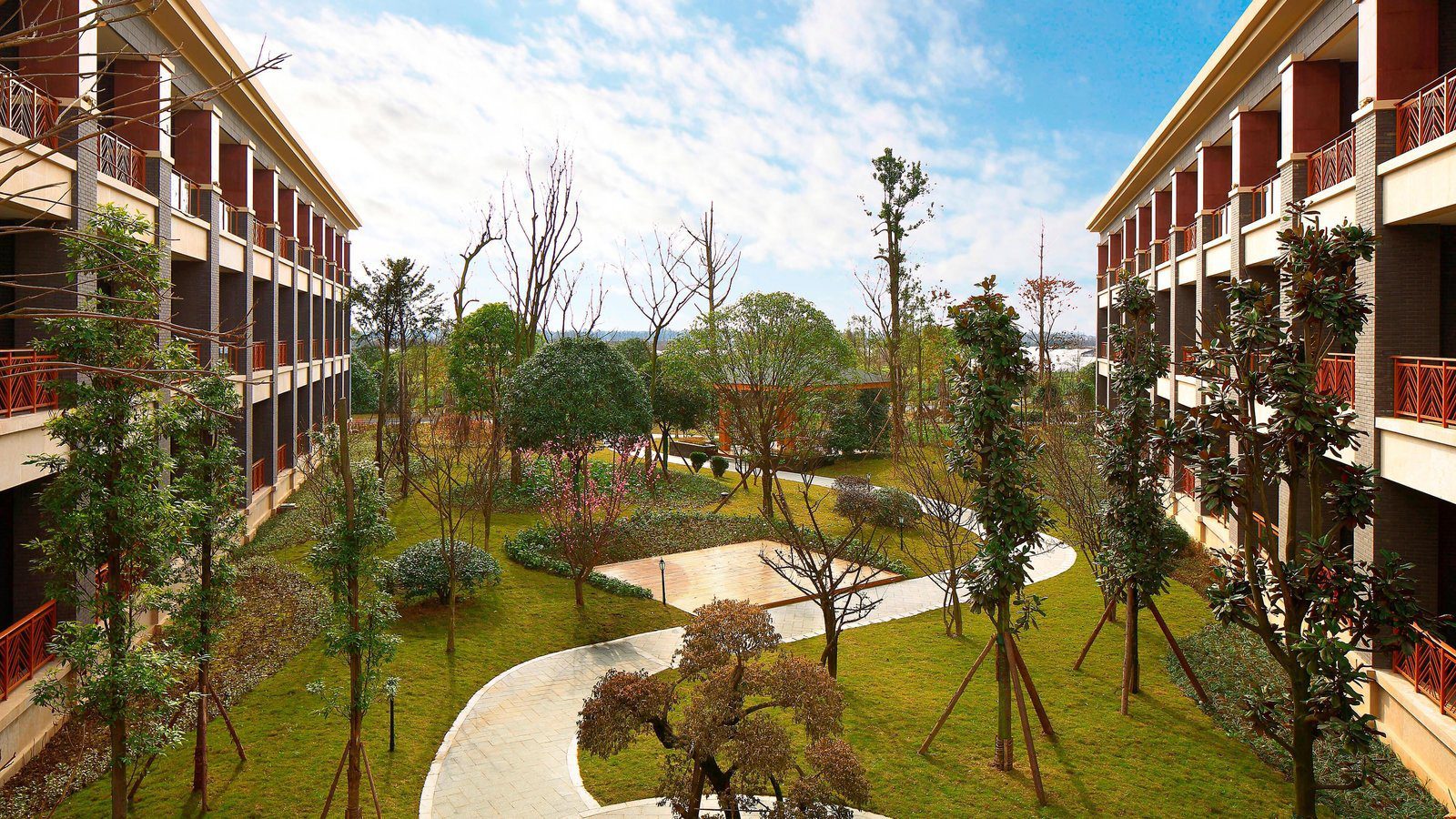 成都安仁福朋喜來登酒店的庭園,兩排帶陽台的三層客房樓之間是草坪、樹木與彎曲步道