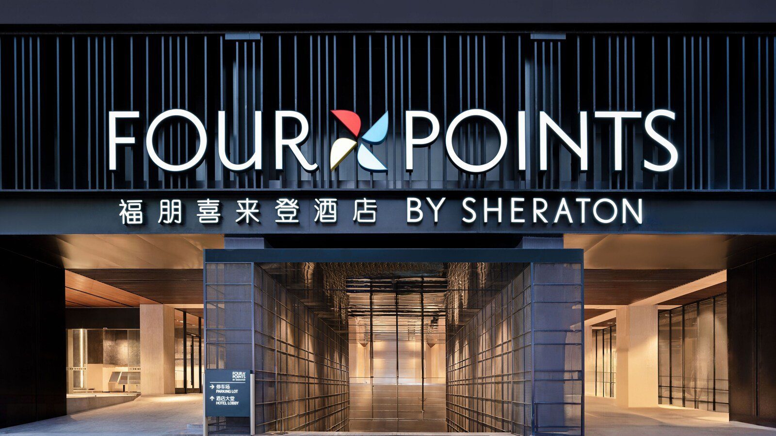 成都春熙路福朋喜來登酒店的入口，黑色格柵牆面上是 FOUR POINTS BY SHERATON 館名招牌，下方玻璃通道通往大堂與停車場