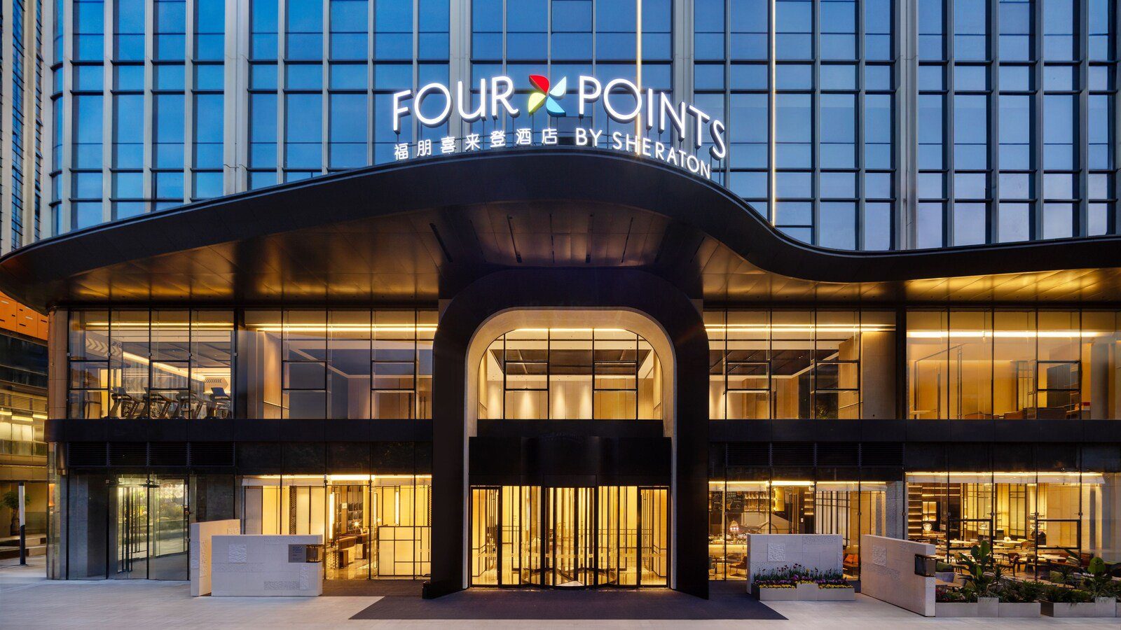 成都東站福朋喜來登酒店的入口夜景,波浪形雨遮上方是 FOUR POINTS BY SHERATON 館名招牌,下方拱形門廊通往旋轉門