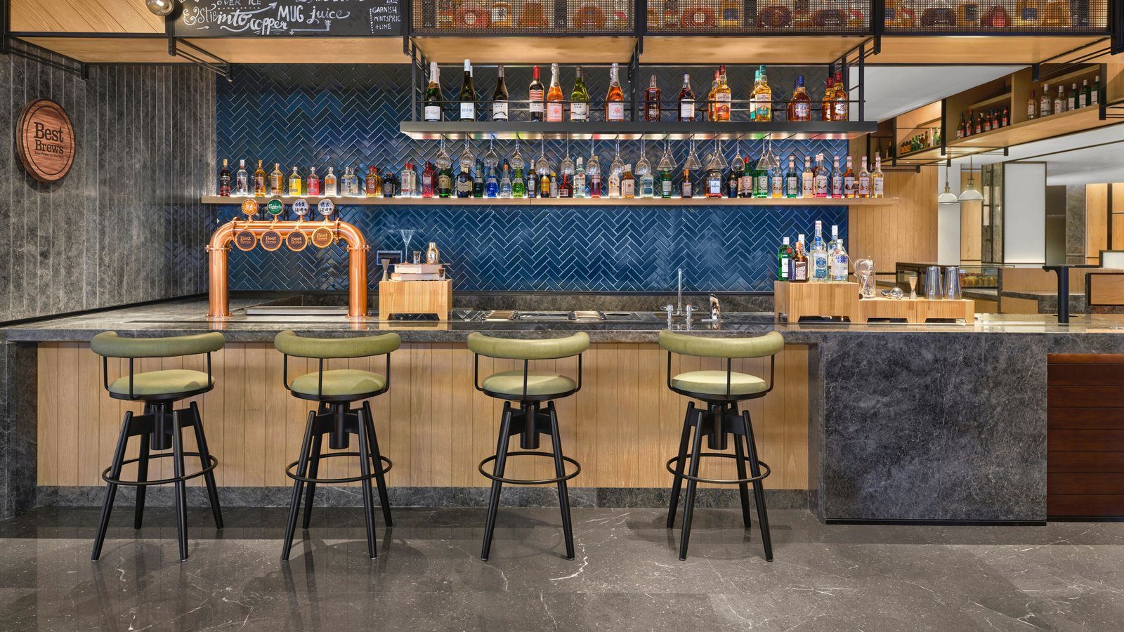 重慶福朋喜來登酒店的 D by THE MESH 吧檯，藍色人字磚牆前的層架擺滿酒瓶，吧檯上有銅色啤酒拉霸，前方排著綠色高腳椅