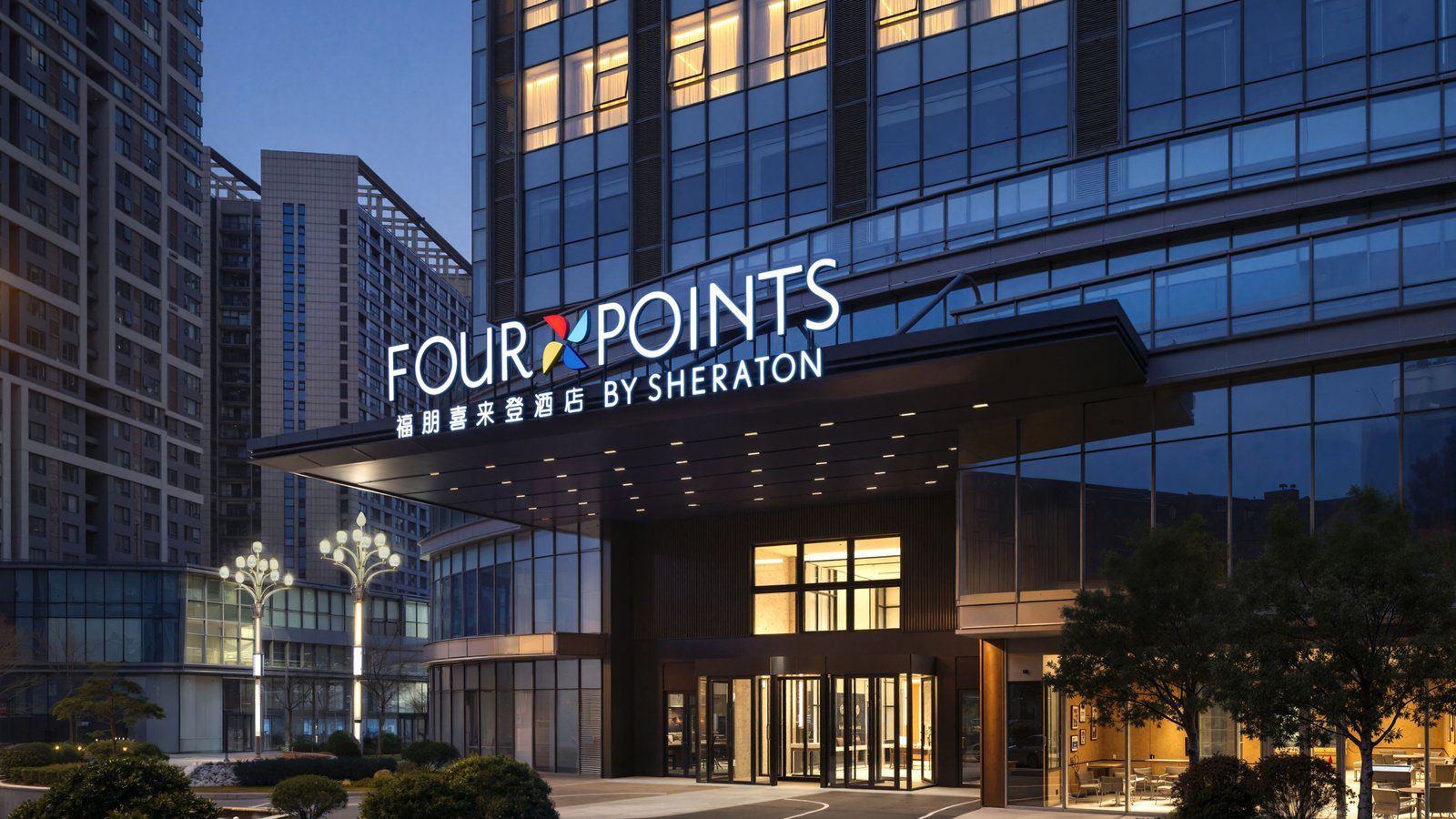 重慶九龍坡福朋喜來登酒店的入口夜景，雨遮上方是 FOUR POINTS BY SHERATON 館名招牌，下方是玻璃門與亮燈的大堂