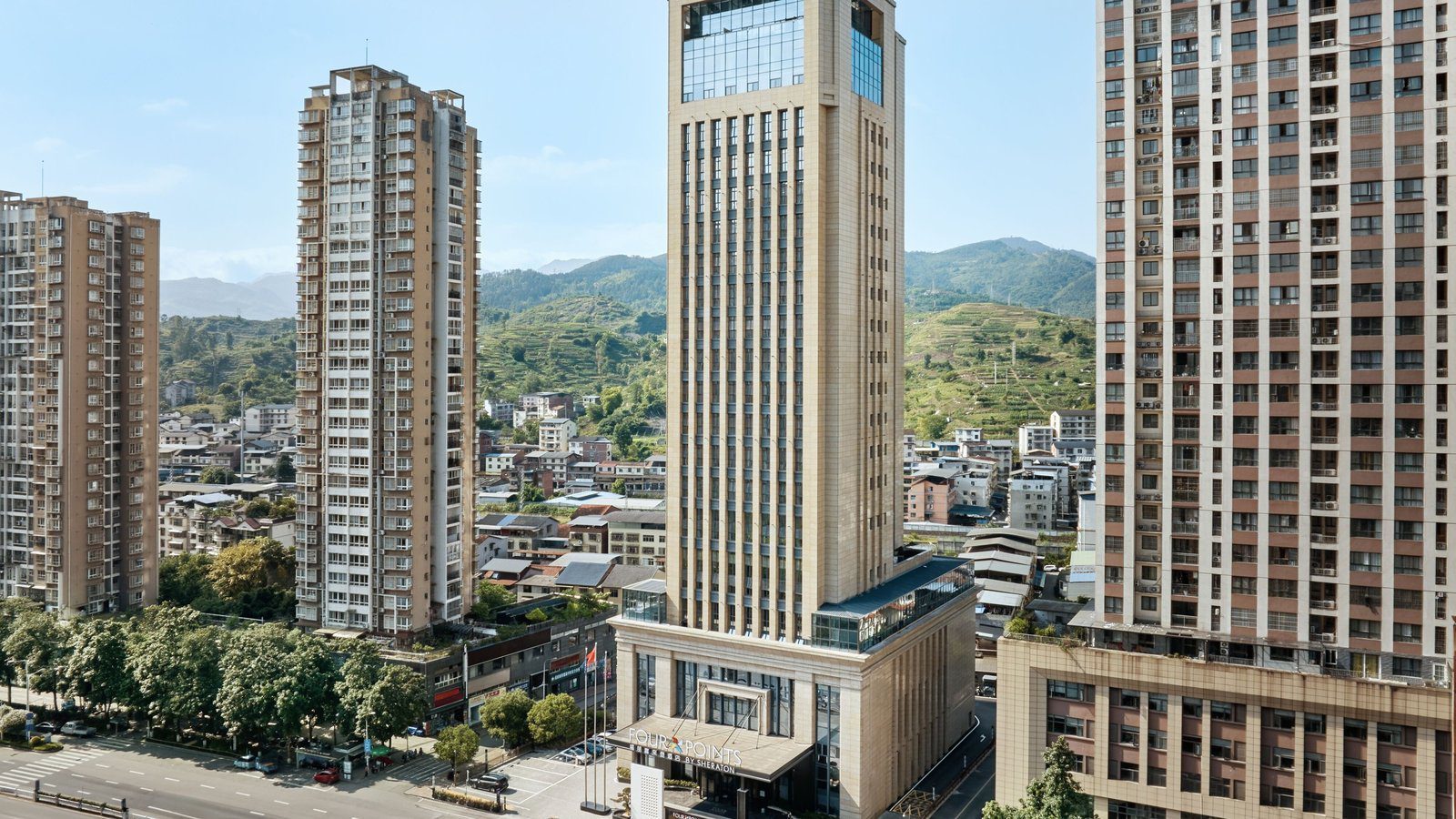 重慶南川福朋喜來登酒店白天外觀，米色塔樓立在南川城區的住宅高樓之間，背後是綠色山巒