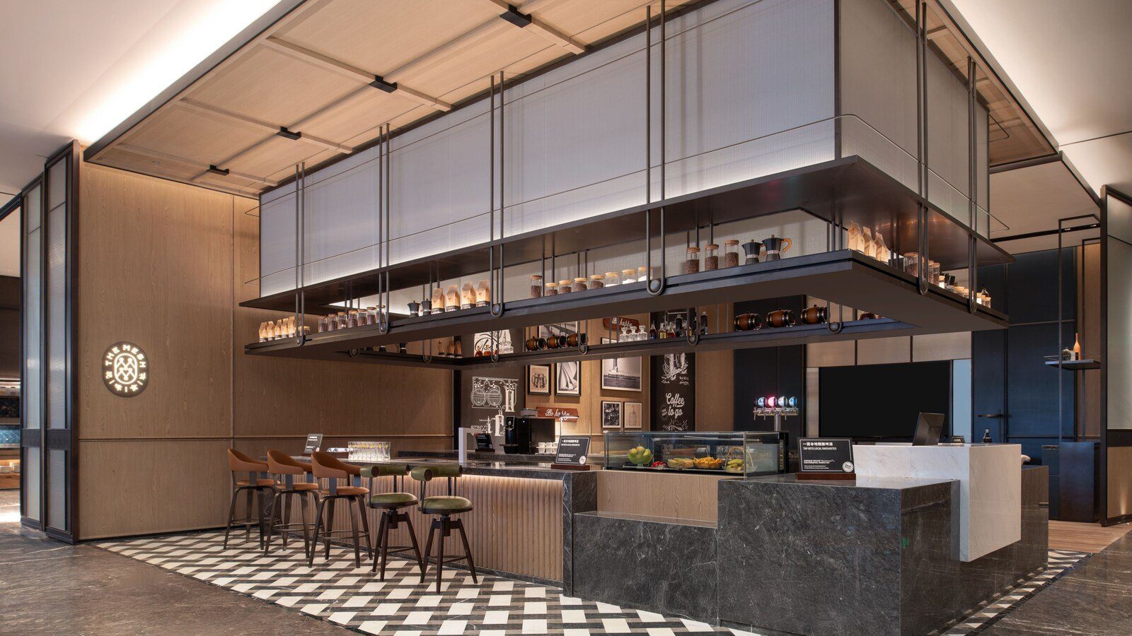 大連東港福朋喜來登酒店玩啤食社 The Mesh 的吧台，懸吊層架上擺著咖啡豆罐與酒桶，吧台前是高腳椅，左側牆上有 THE MESH 圓形標誌