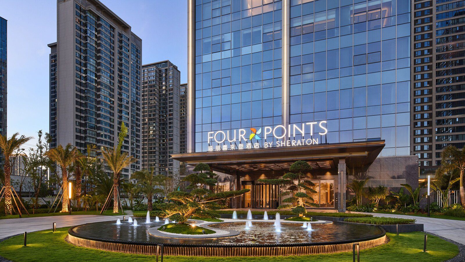 昆明長晟福朋喜來登酒店的入口,雨遮上方是 FOUR POINTS 招牌,前方是圓形噴水池、造型松與棕櫚樹