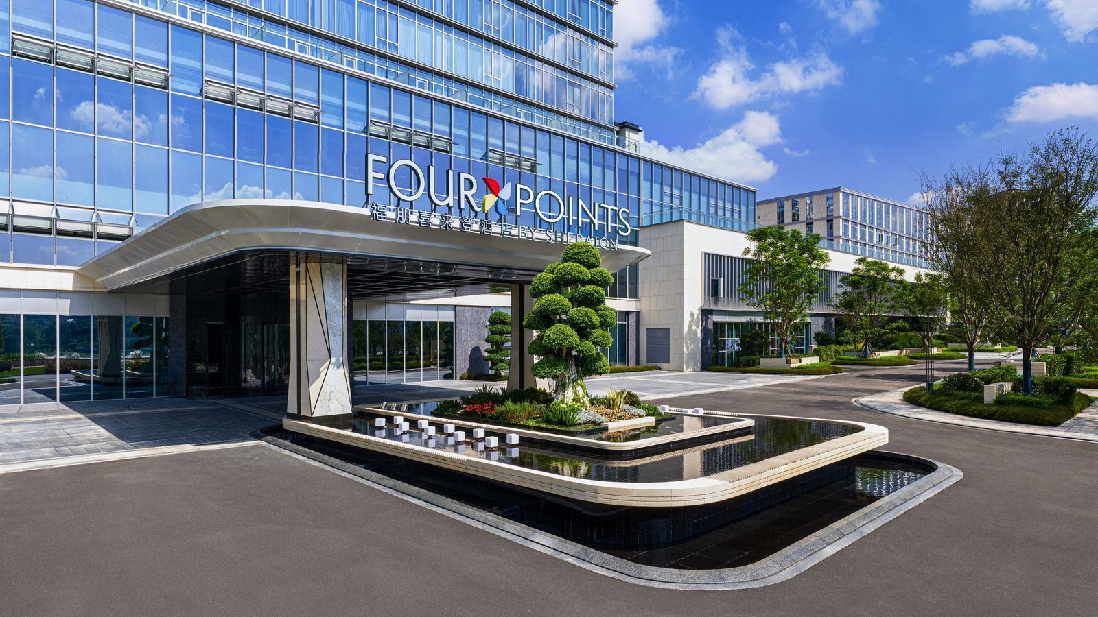 樂山福朋喜來登酒店入口，弧形雨遮上方是 FOUR POINTS 館名招牌，門前是造型松樹與水景