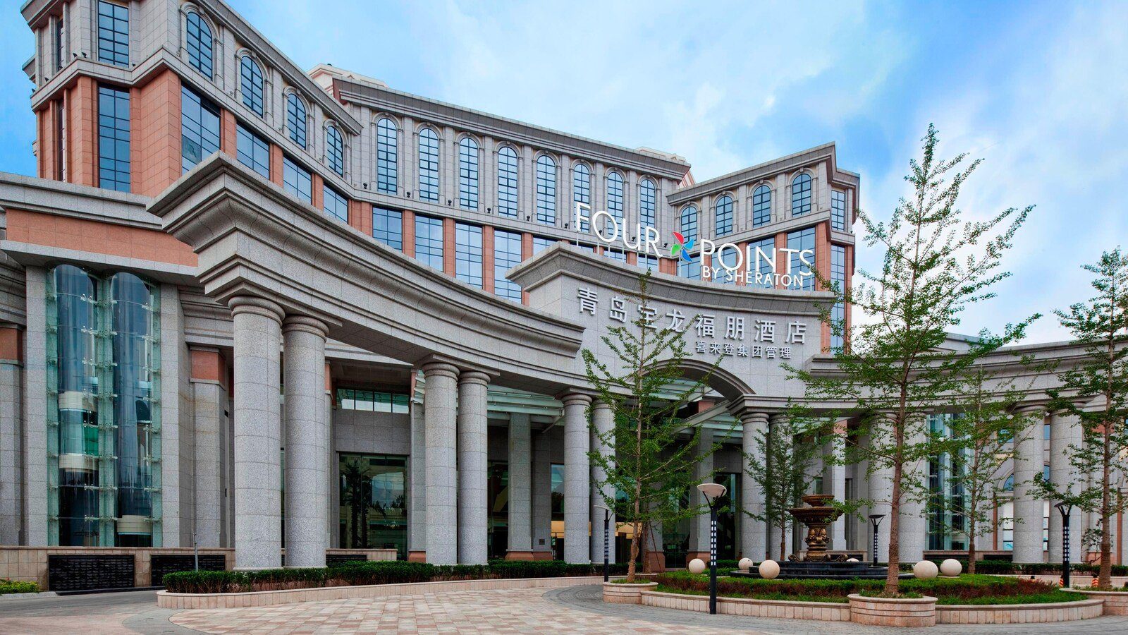 青島城陽寶龍福朋喜來登酒店側面外觀，石柱廊與車道旁種著銀杏樹，樓頂是 FOUR POINTS 招牌