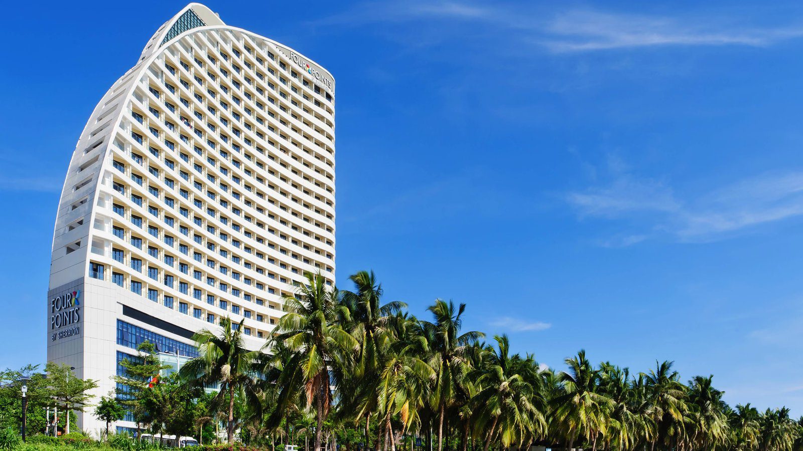 三亞福朋喜來登酒店的白色弧形塔樓，底座與頂部有 FOUR POINTS BY SHERATON 招牌，前方是一排椰子樹