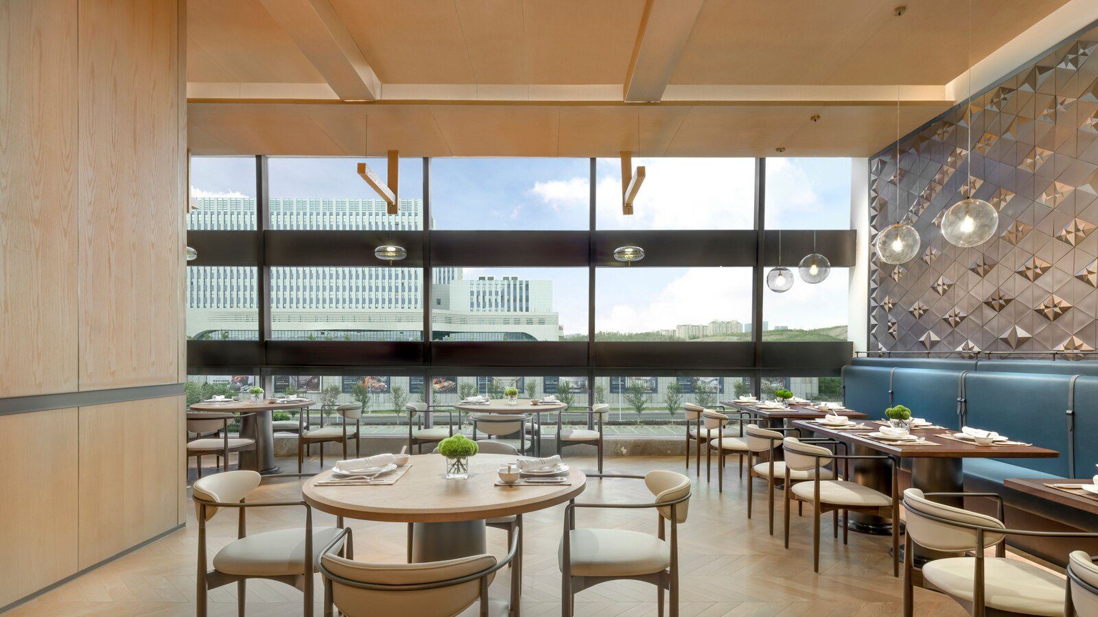 烏魯木齊中建福朋喜來登酒店華韻中餐廳，淺色木頭天花板下擺著圓桌與方桌，右側是藍色長沙發與幾何立體牆面，整面玻璃窗外是白色建築與綠地