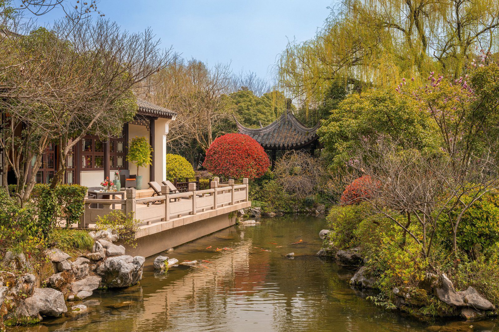 杭州西子湖四季酒店庭園水塘旁的石欄露台與躺椅，對岸是灰瓦涼亭與紅葉灌木