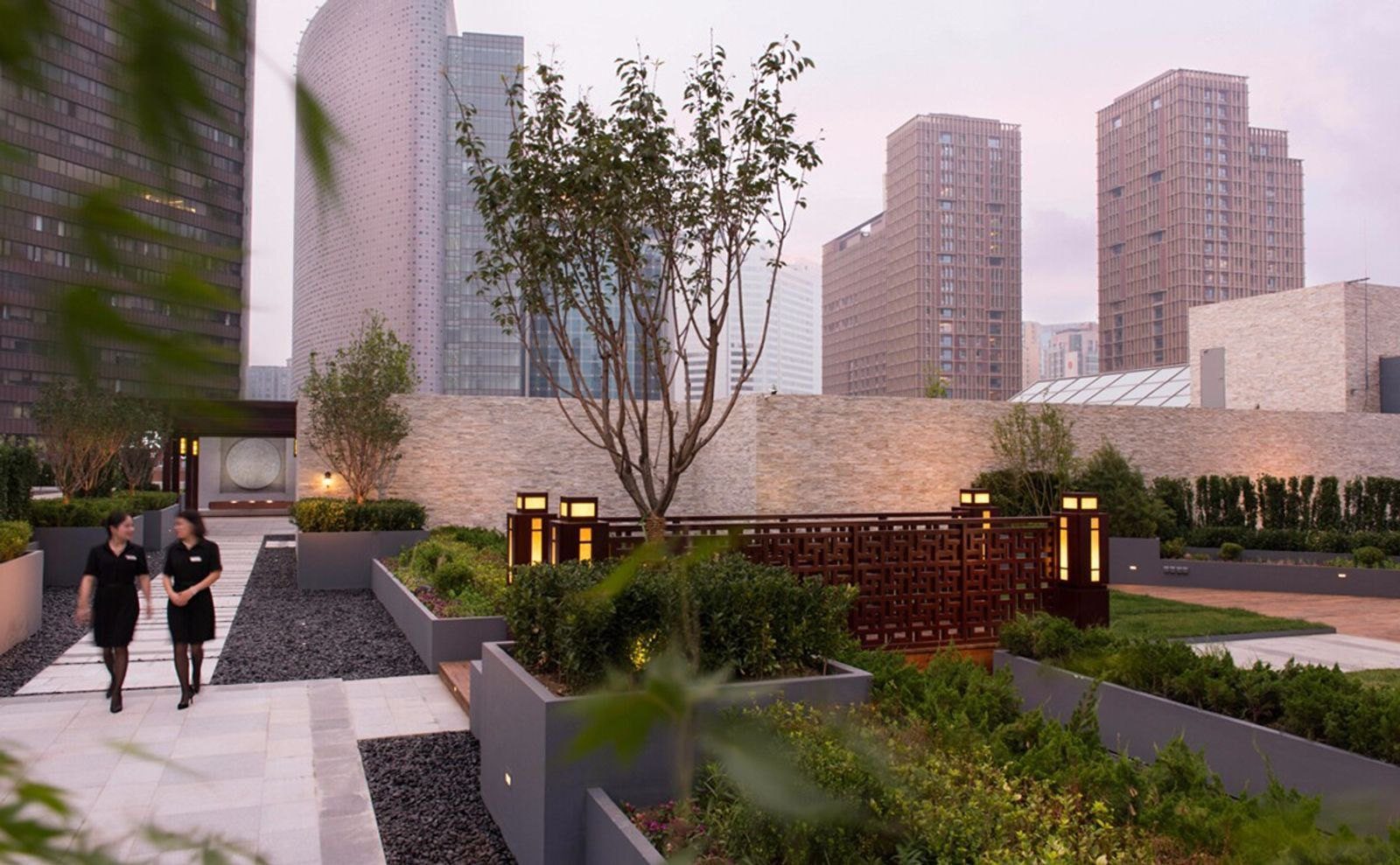 北京希爾頓酒店的空中花園,花台與步道之間種著綠樹,兩位員工沿步道走過,後方是周邊的高樓