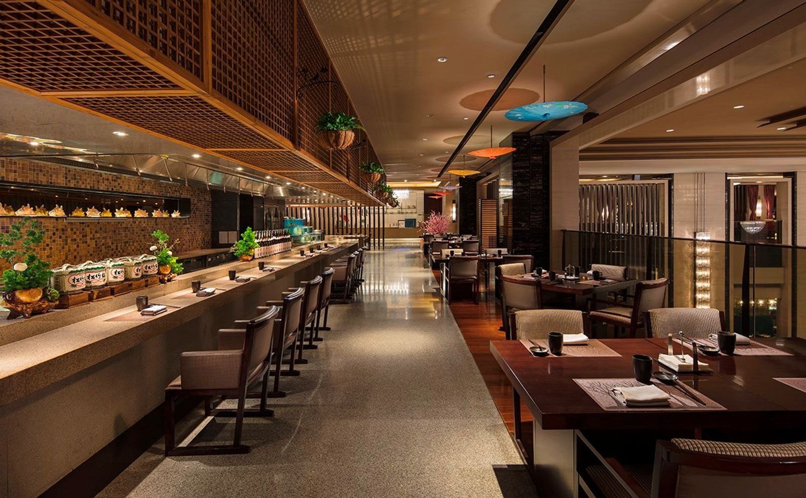 大連富力希爾頓酒店源氏餐廳，左側是長條料理吧台與一排高背椅，上方是木格柵，右側是鋪著餐墊的方桌與懸掛的紙傘