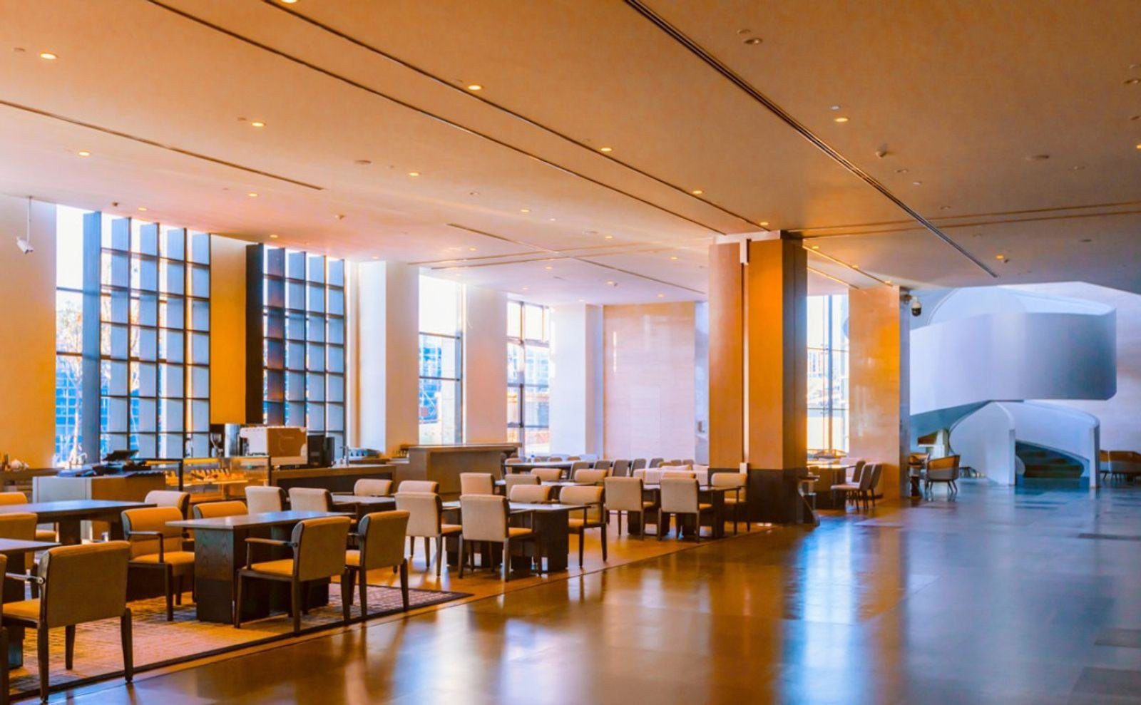 麗江晶璽希爾頓酒店的全日制餐廳，挑高空間排著米色餐椅與深色餐桌，左側是高大的格子窗，右側是白色螺旋樓梯