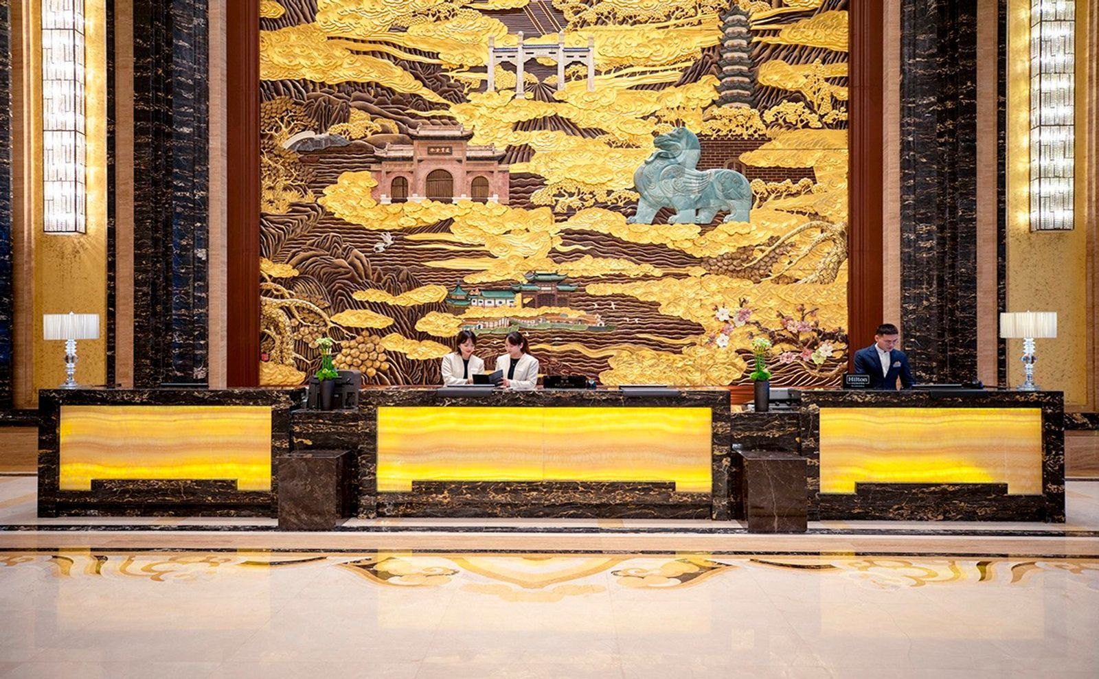 南京希爾頓酒店的接待櫃檯,發光玉石面板的櫃檯後方是金色南京山水浮雕,浮雕上有牌坊、古塔與石獸