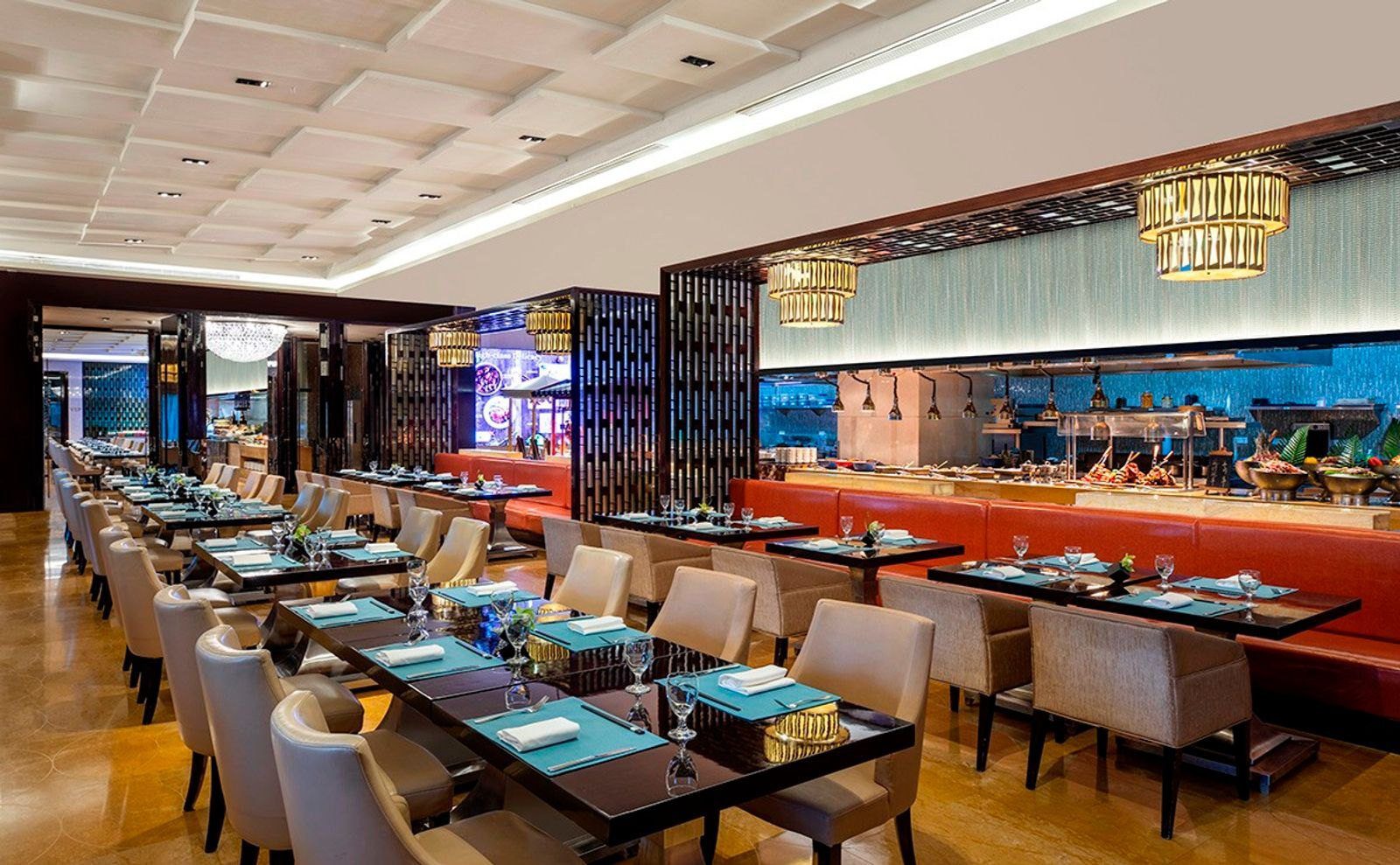 南京希爾頓酒店匯・全日餐廳，深色方桌配米色扶手椅與橘紅色長沙發，後方是亮燈的開放式廚房與自助餐檯