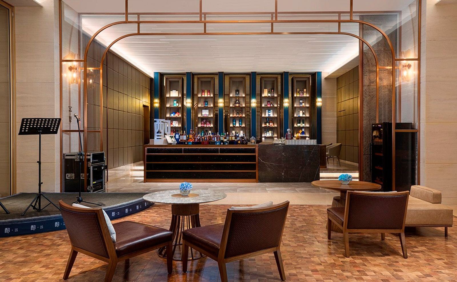南京希爾頓酒店 Z Bar，銅色拱形框架後是深藍色酒櫃與黑色吧檯，左側小舞台上擺著譜架與麥克風