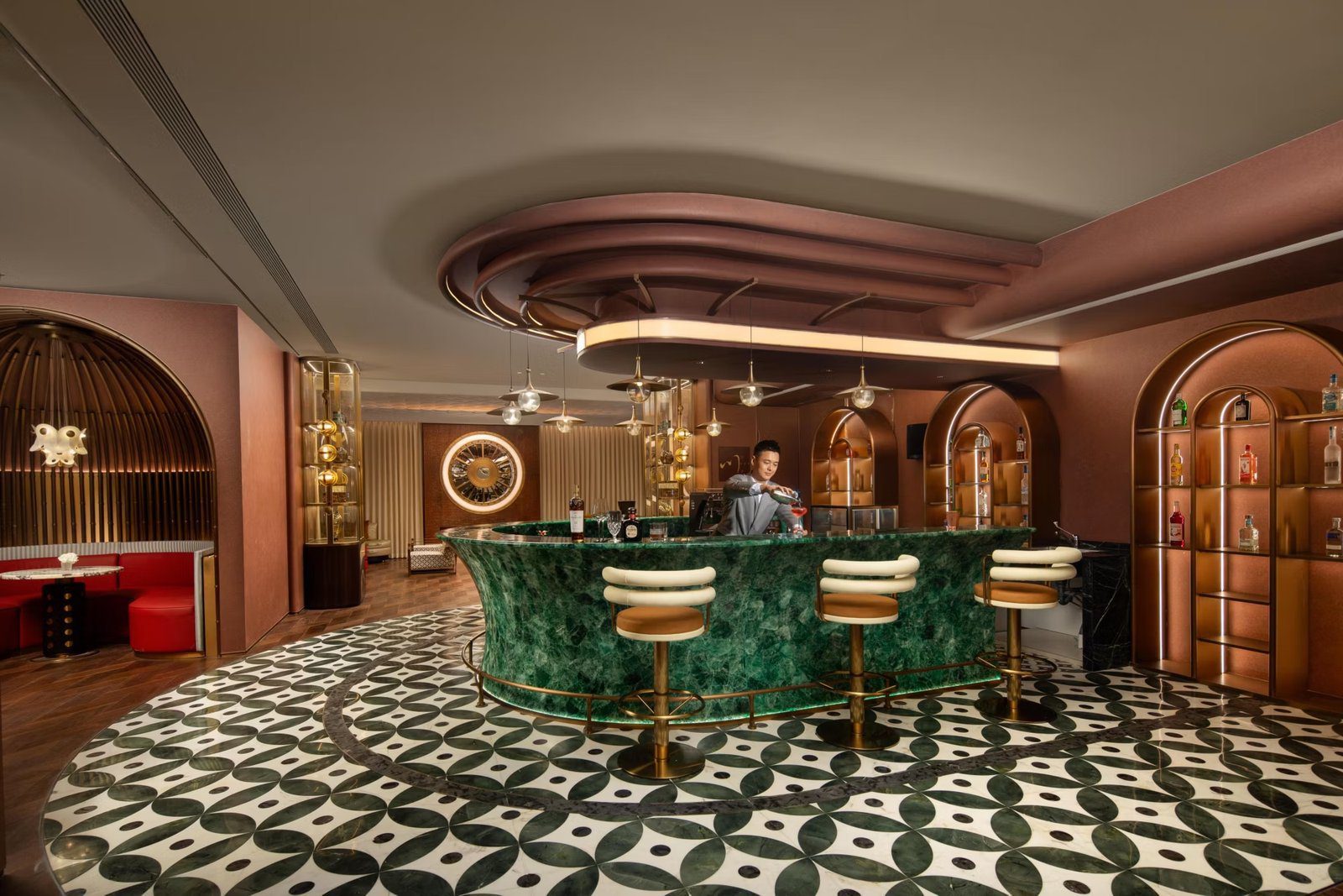 成都金融城英迪格酒店 MEET 川行大堂吧的綠色大理石弧形吧台與皮革吧椅，粉橘色牆面上有圓拱造型酒櫃，地坪是黑白幾何花磚，吧台後有一位調酒師在調飲