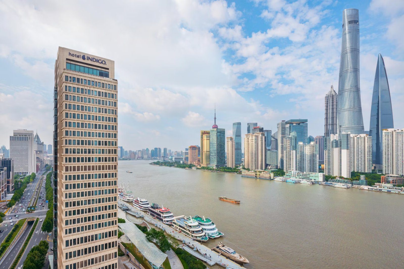 上海外灘英迪格酒店白天的建築側面,右側是黃浦江、碼頭停靠的遊船與對岸陸家嘴天際線