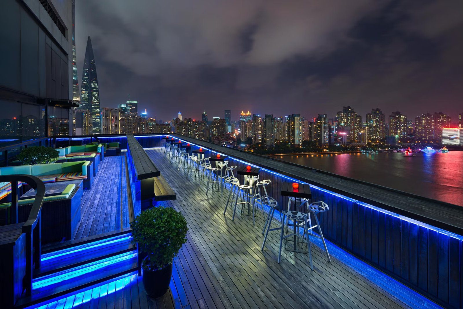 上海外灘英迪格酒店頂樓露台酒吧夜景，木質露台的藍色地燈、高腳桌椅與對岸城市燈火