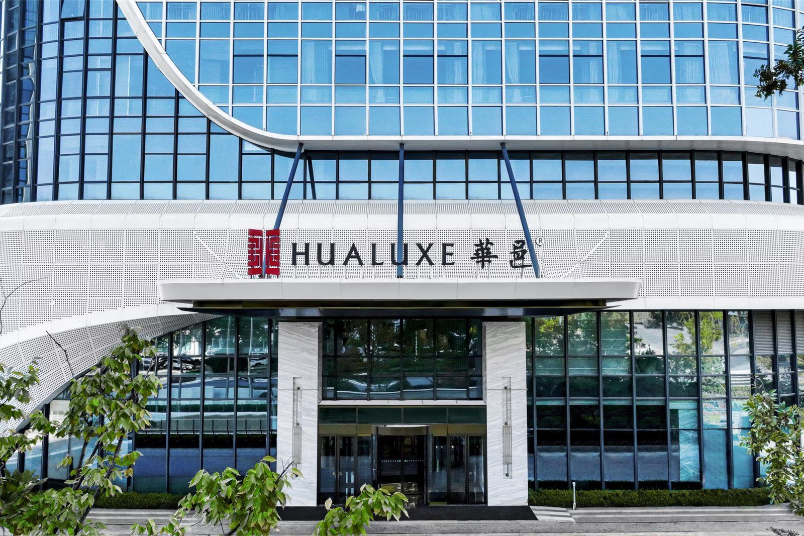 青島李滄華邑酒店主入口，白色雨庇上方是紅色印章標誌與 HUALUXE 華邑字樣